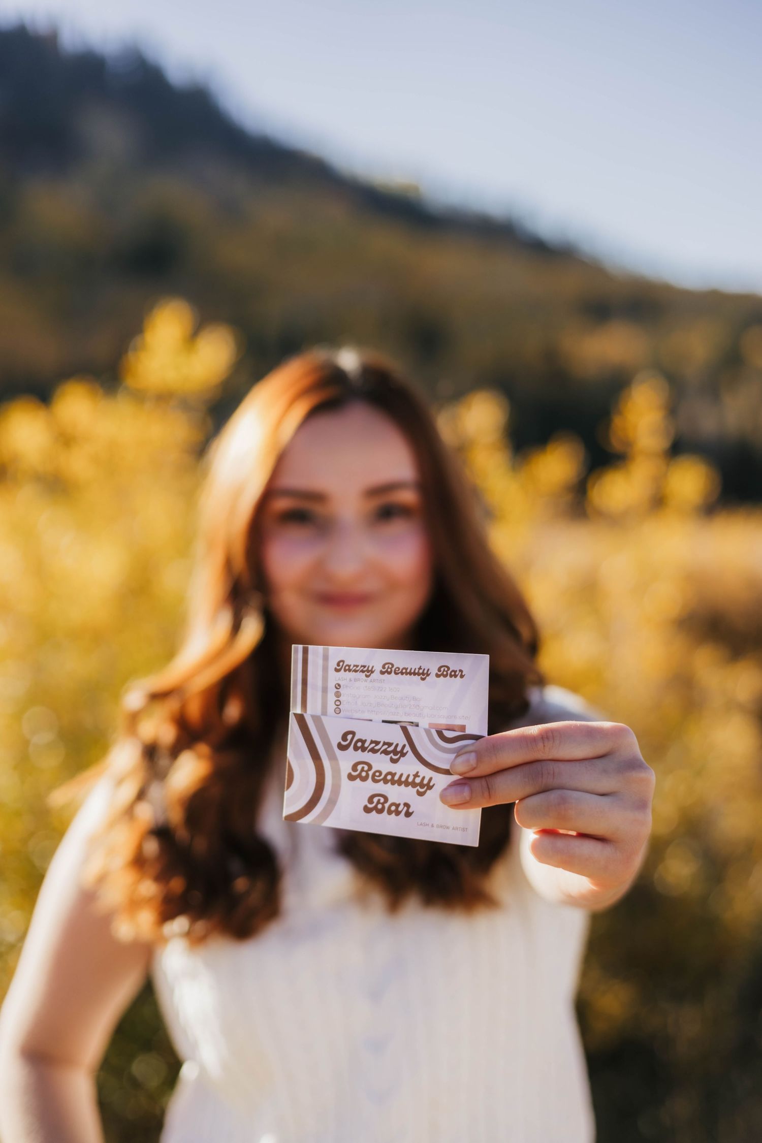 A person holding up business cards in front of autumn foliage with golden sunlight.