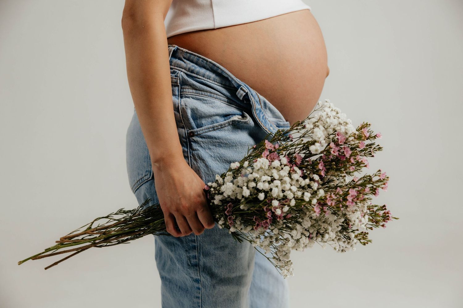 Maternity photos with dried flowers against neutral studio background showing growing baby bump.