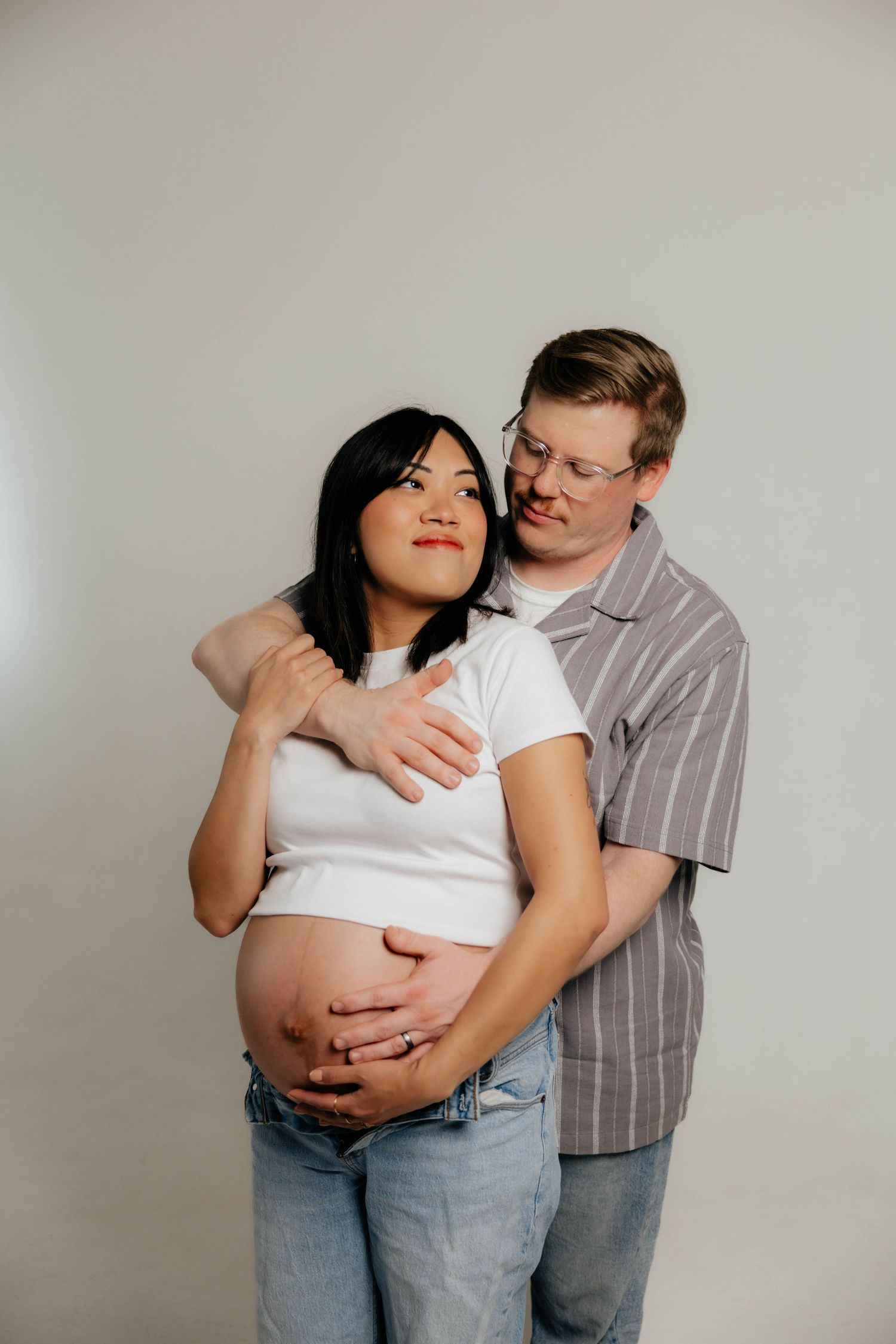 Minimalist studio maternity photos featuring casual denim and white shirt styling.
