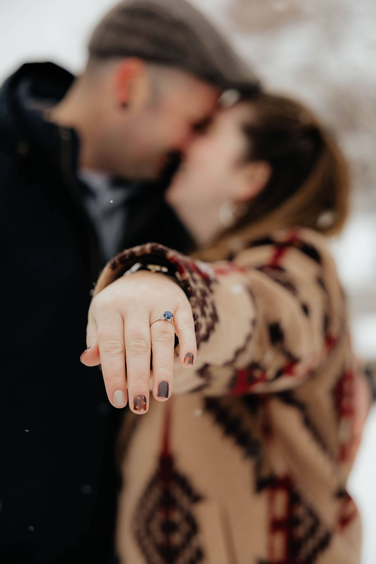 Close-up of engagement ring with couple embracing in soft focus background.