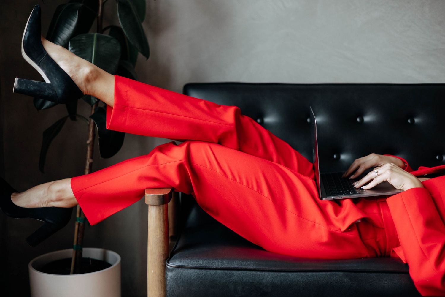 Person in red clothing reclining on dark furniture in dramatic lighting.
