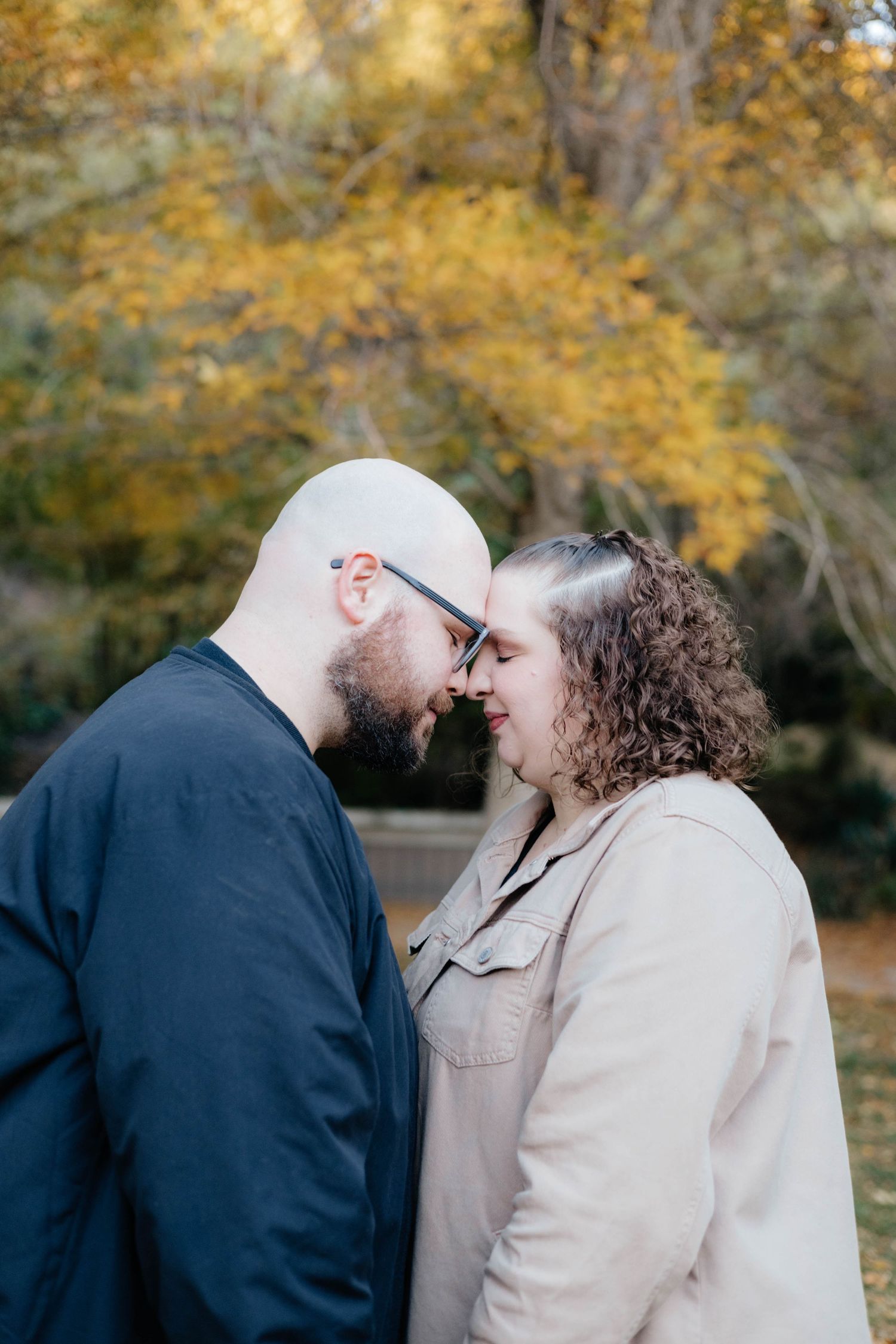Intimate portrait of couple embracing in fall park setting with golden foliage.