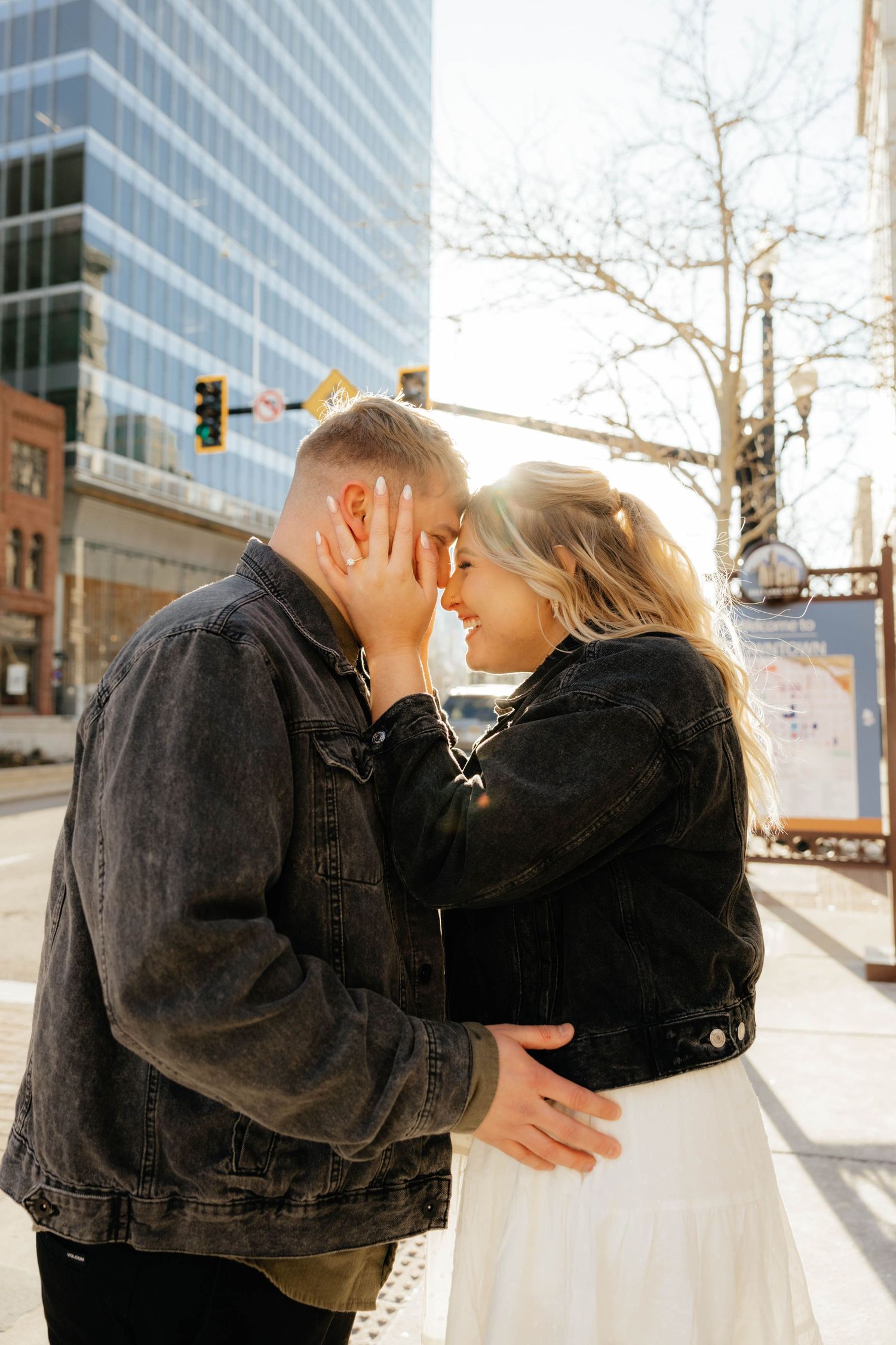 Romantic couple embracing in urban setting with modern buildings in background.