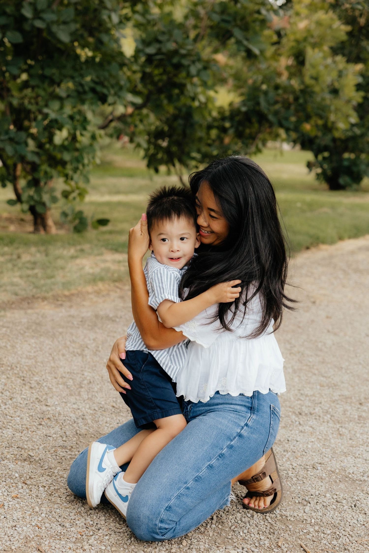 Tender outdoor family moment captured on a dirt path under trees.