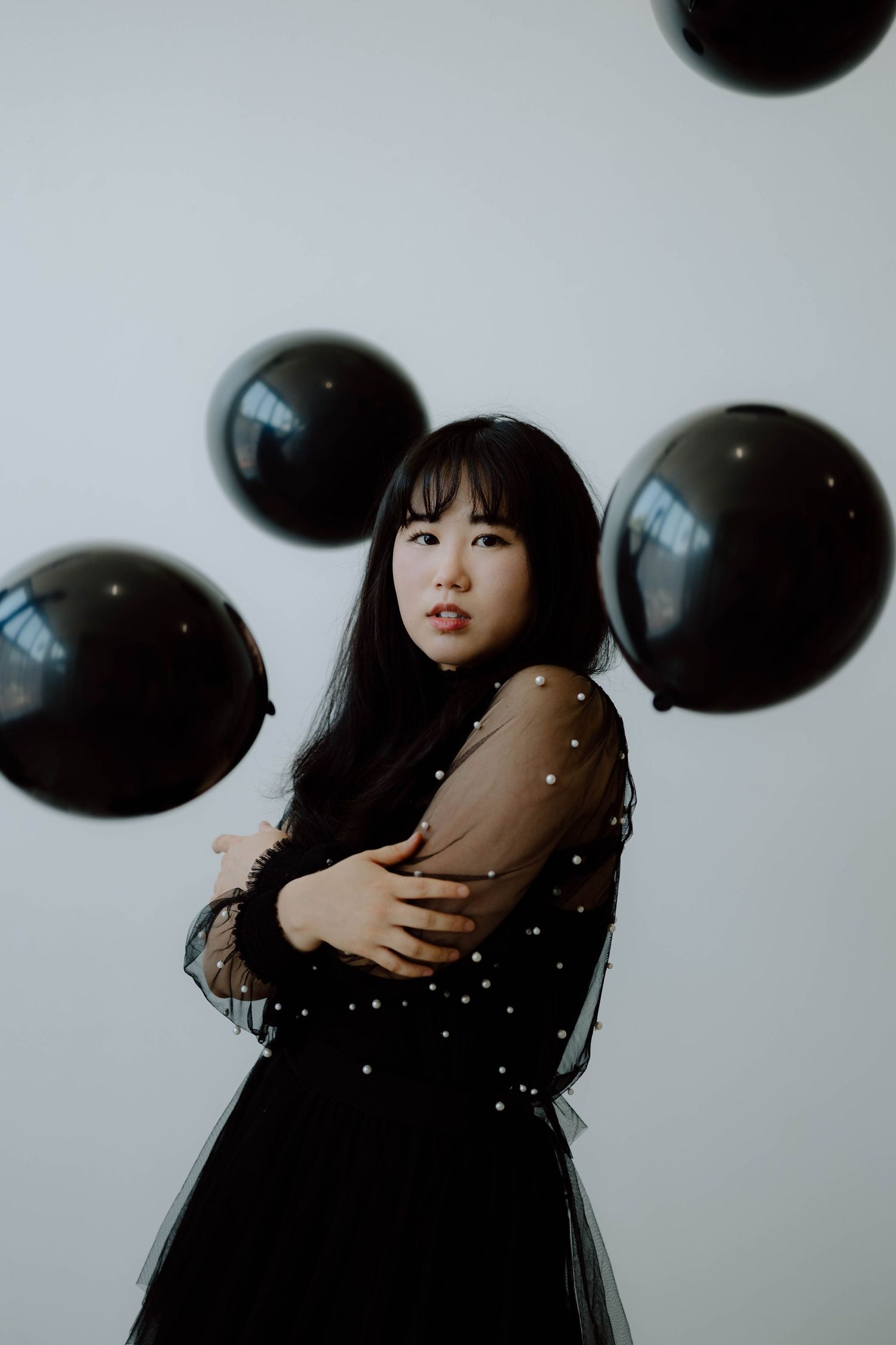 Artistic portrait with floating black balloons and sparkles against white background.