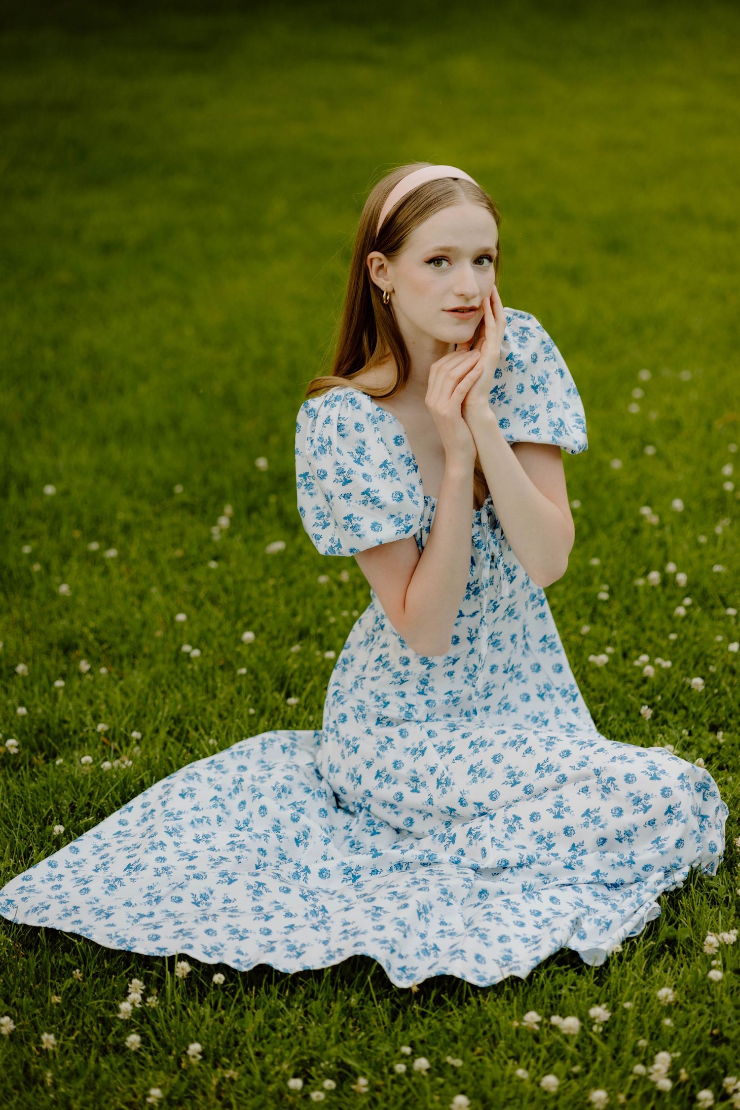 Romantic portrait in a blue floral dress sitting in a blooming meadow.