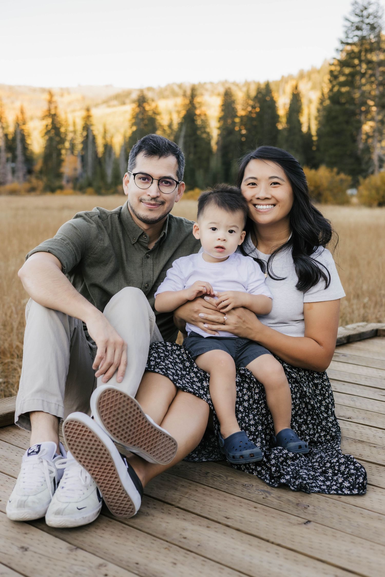 Family sitting together on wooden deck surrounded by fall mountain scenery.