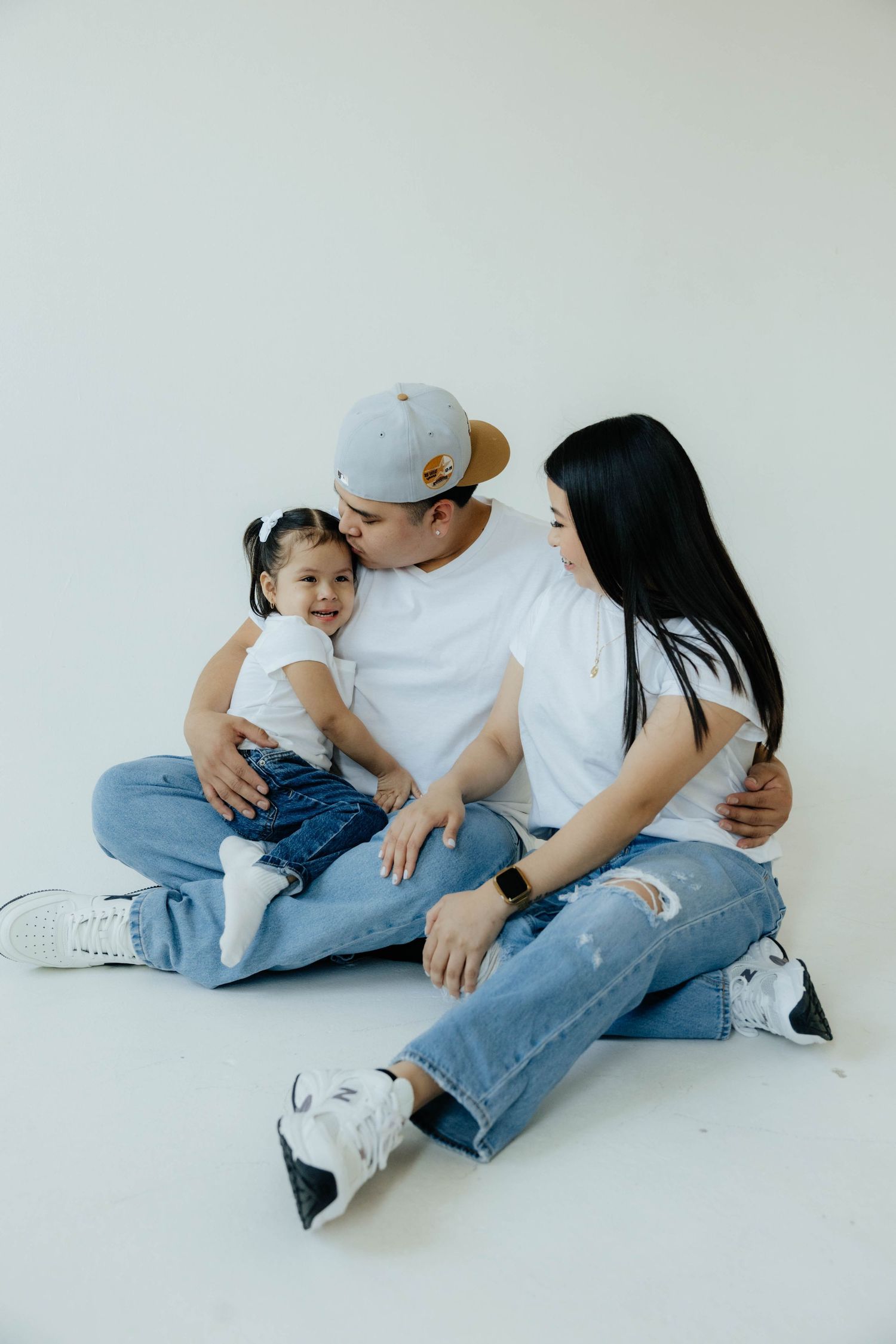 A casual family portrait session with matching white shirts and blue jeans on a white background.