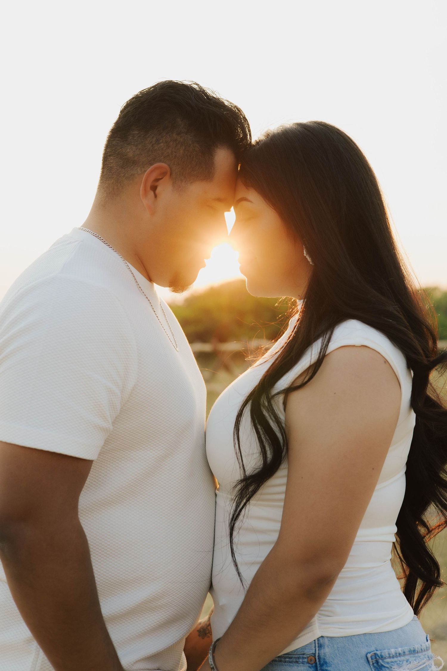 Romantic sunset photoshoot of couple in white shirts creating silhouette against golden light.
