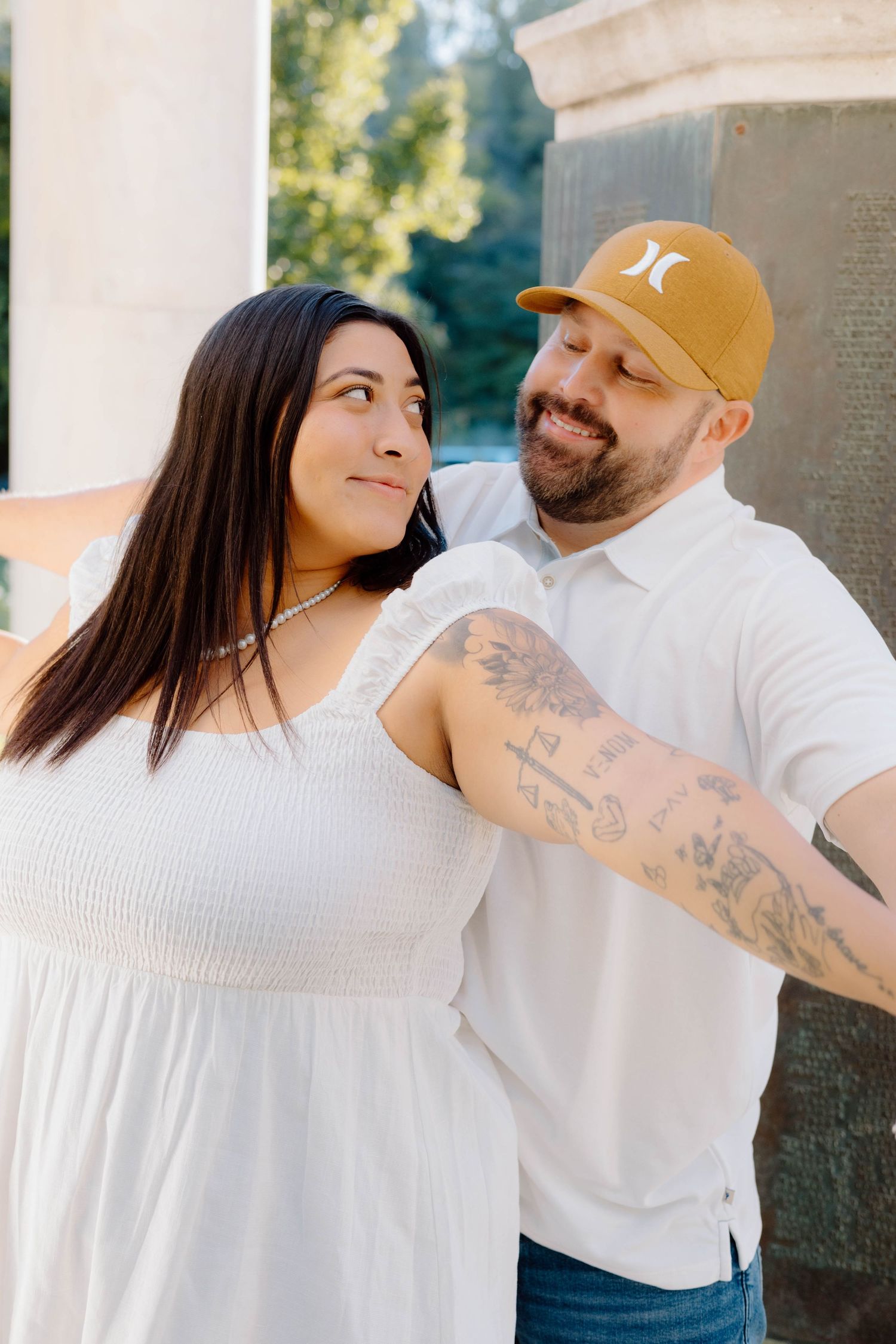 Couple in white outfits playfully posing against stone wall outdoors.