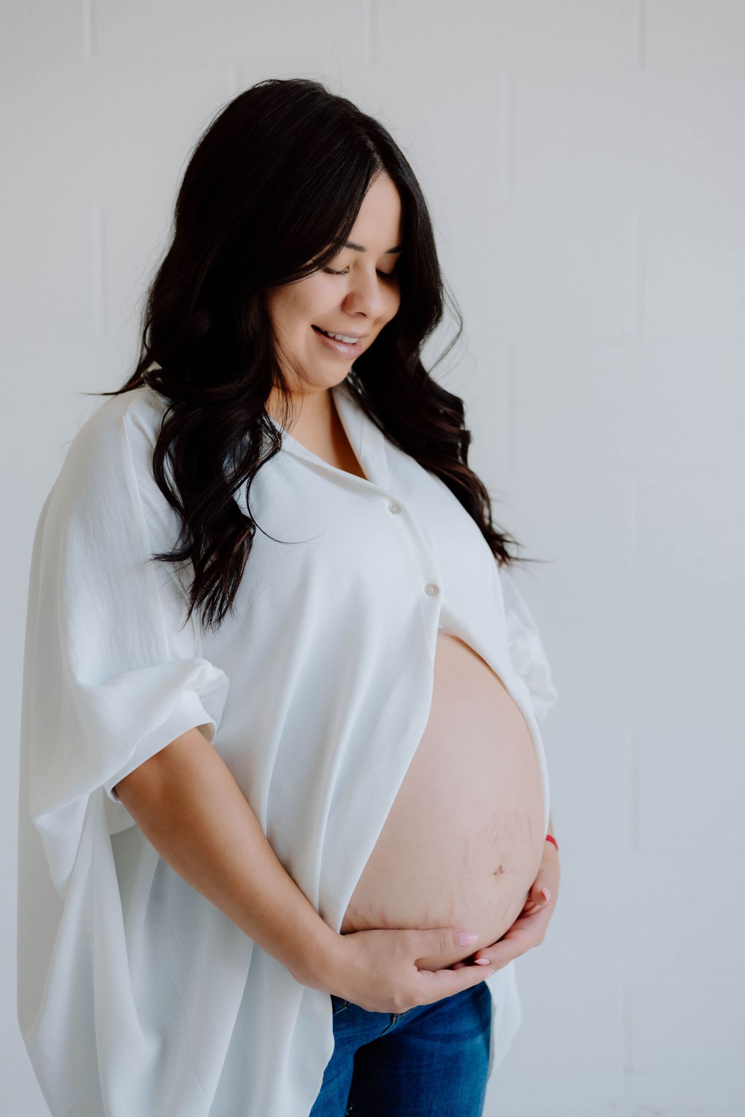 Minimalist maternity photos featuring a white shirt and jeans against a light backdrop.