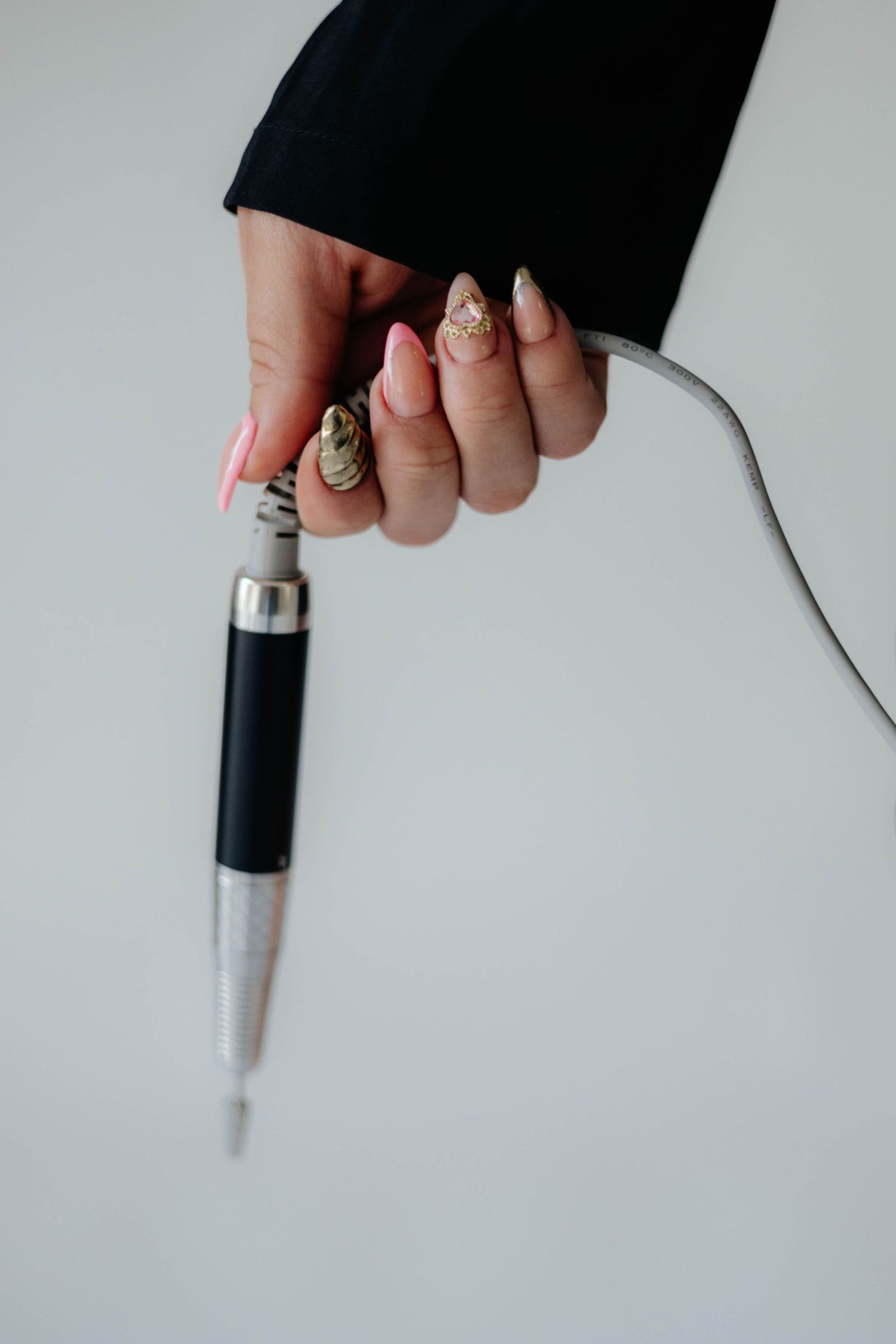 Close-up of manicured hand holding a black and silver pen against white background.
