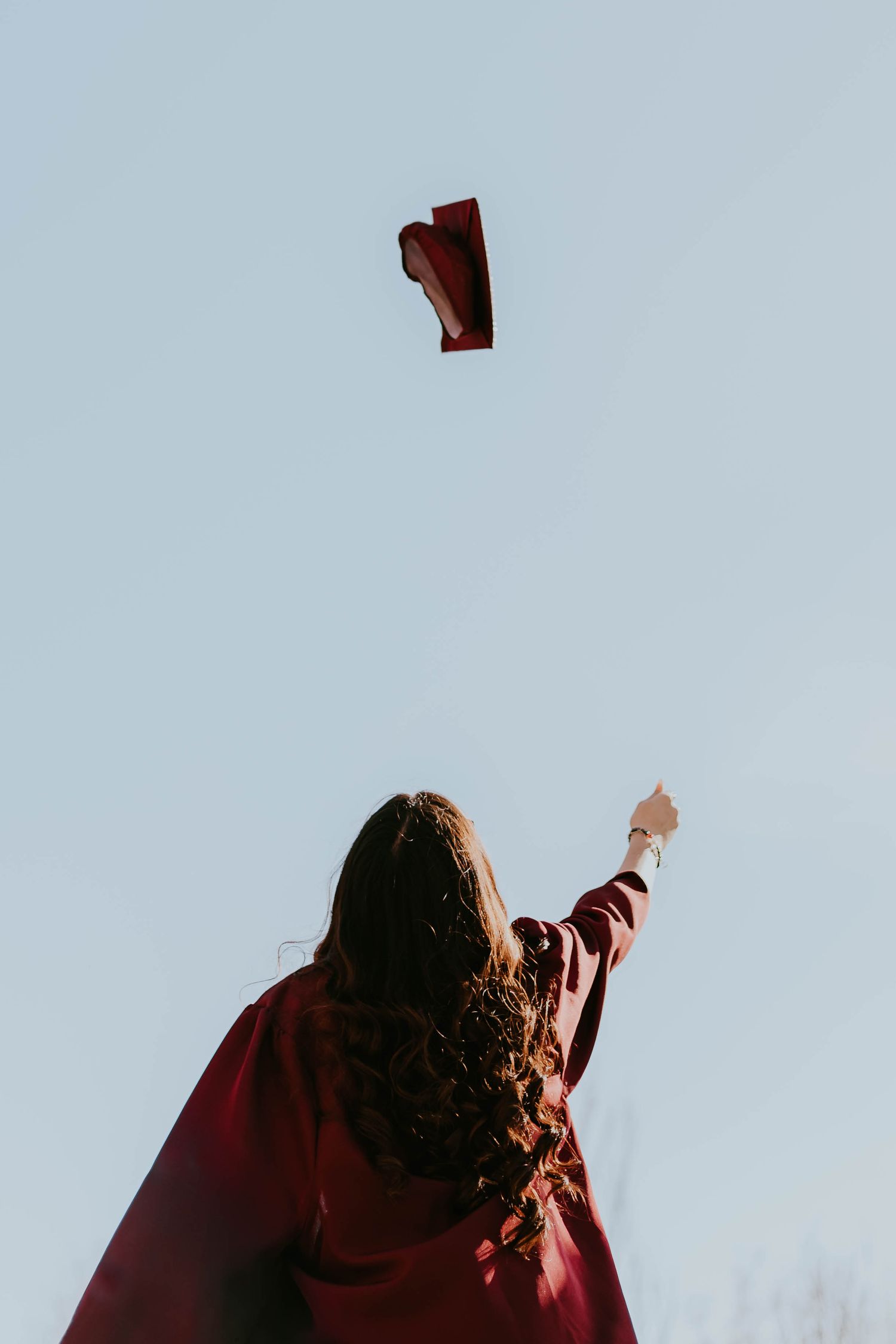 A graduate tosses their red graduation cap into a bright blue sky.