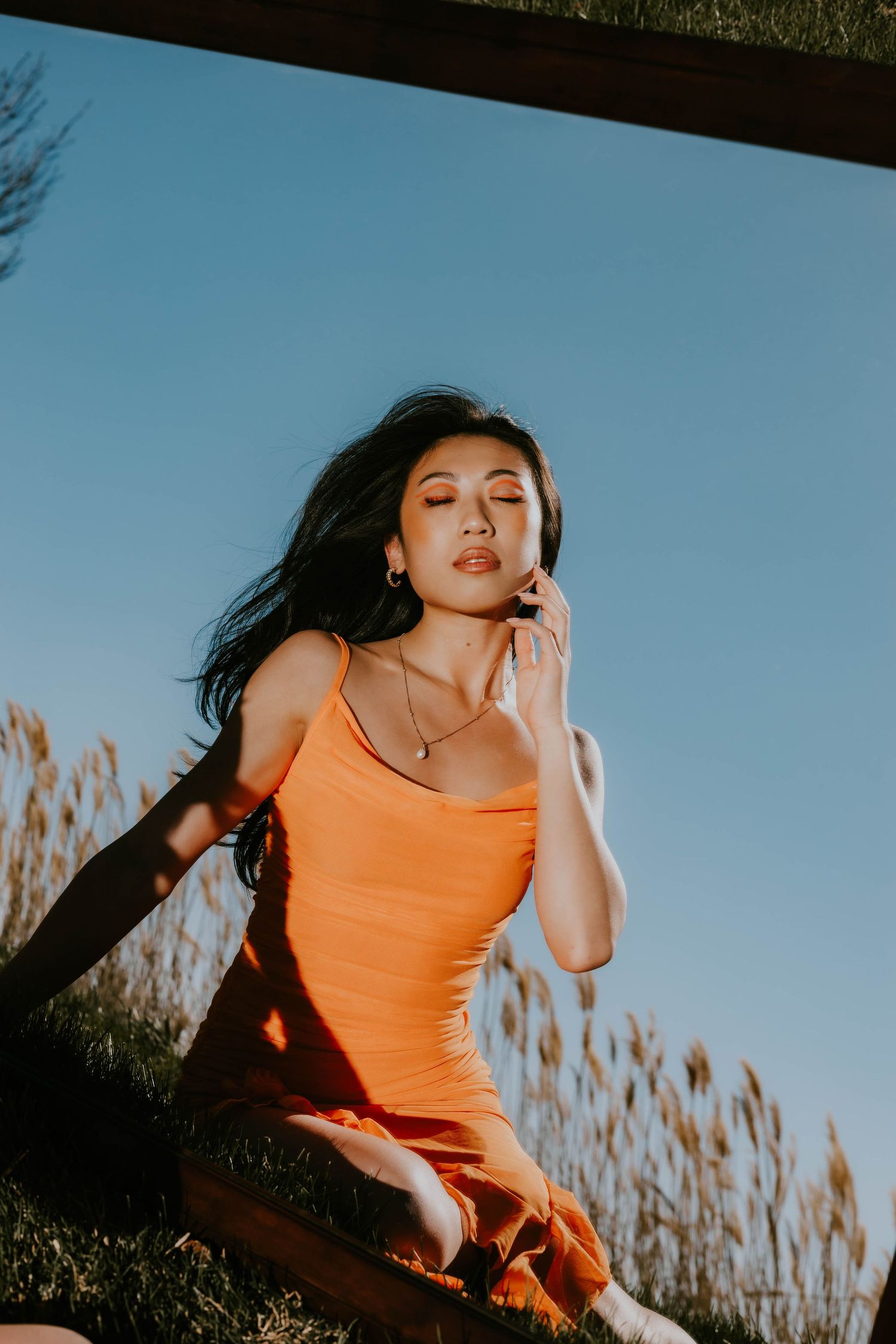 Dynamic portrait in orange tank top against blue sky and tall grass.