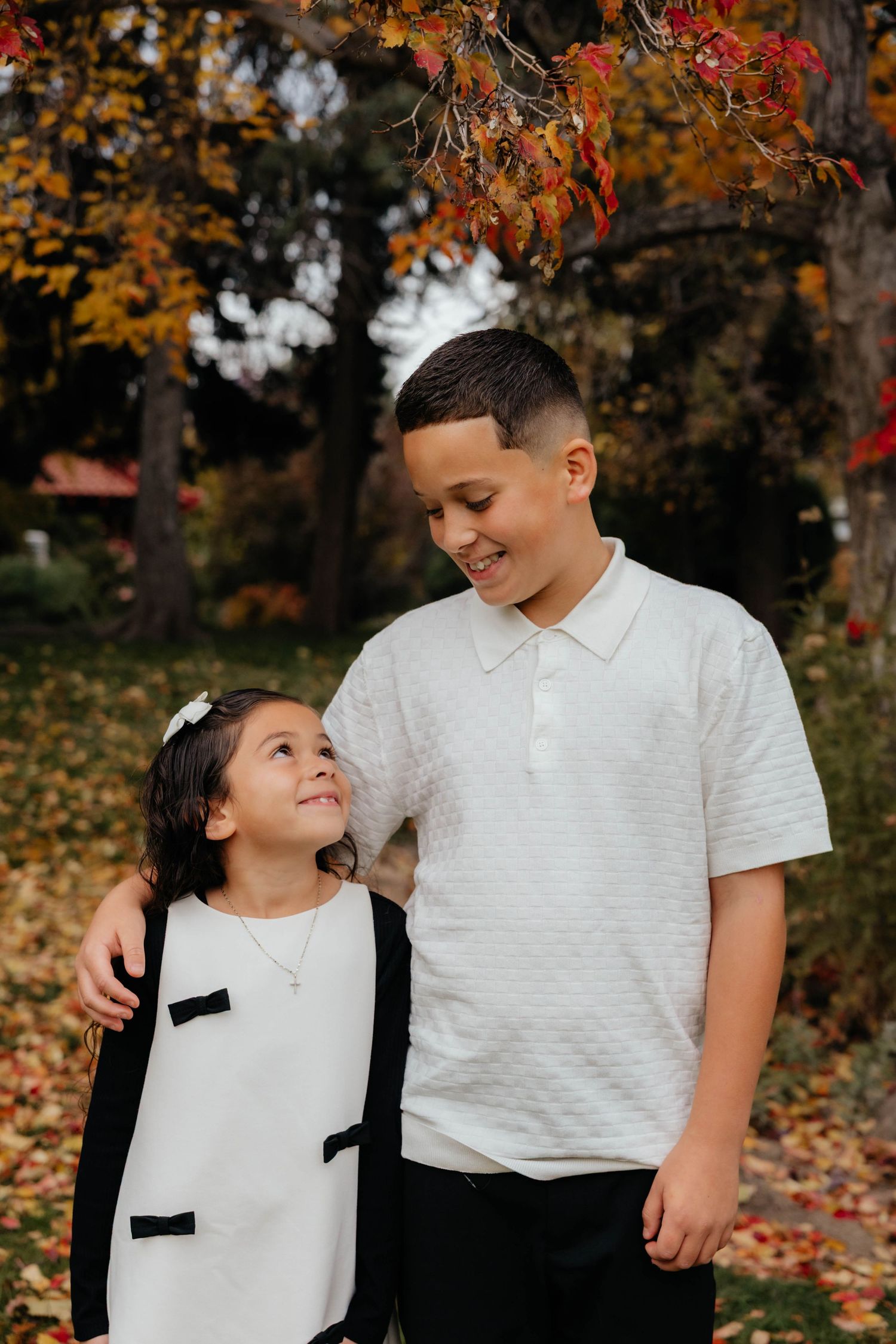 Sweet family moment captured outdoors with autumn leaves in background.