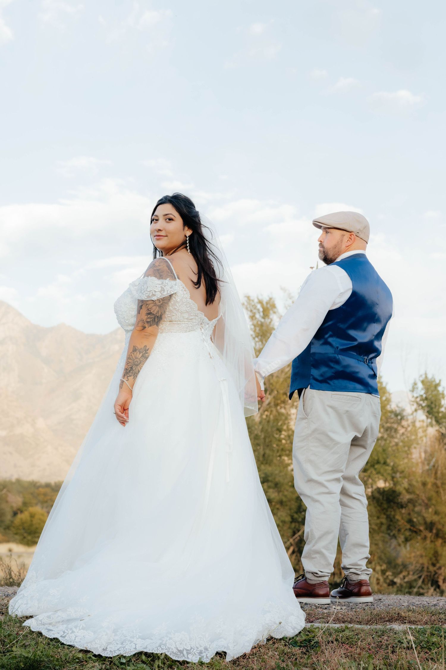 Wedding couple dances playfully in white attire on a desert terrain.