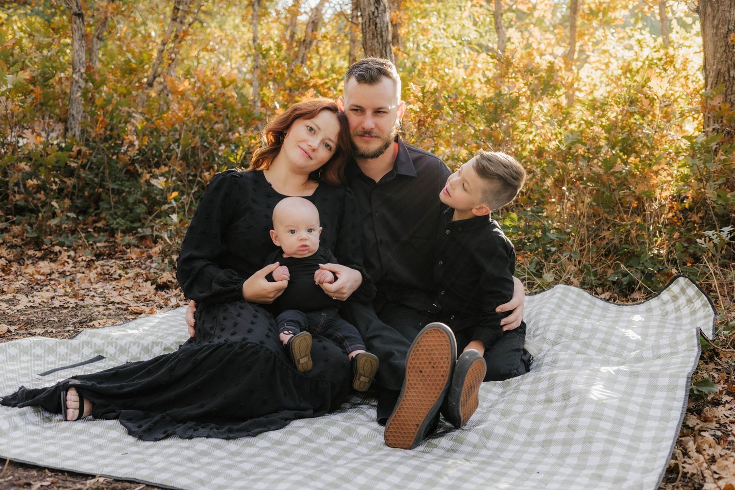 Family enjoying a fall picnic on checkered blanket surrounded by golden autumn leaves.