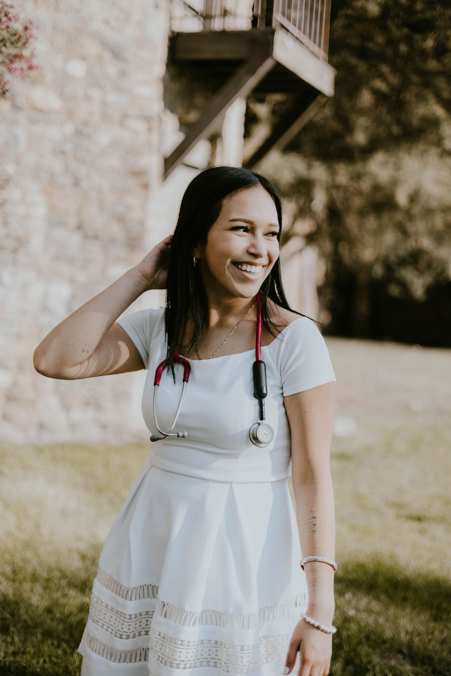 Graduate in white dress and red cap smiles joyfully during outdoor photo session.