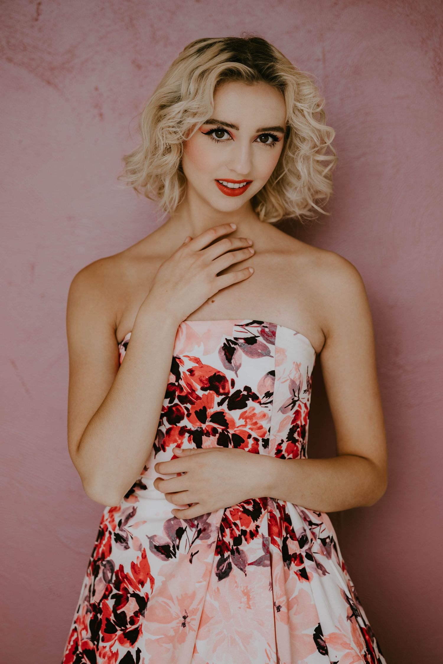 Portrait against pink wall wearing floral dress with red and pink flowers.
