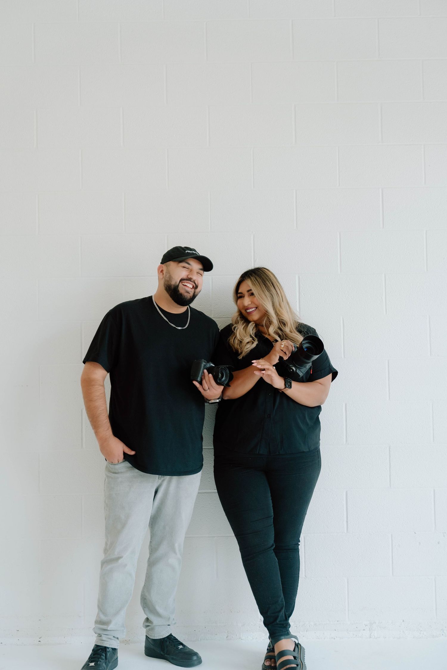 Fun studio session showing couple in matching black outfits against white background.