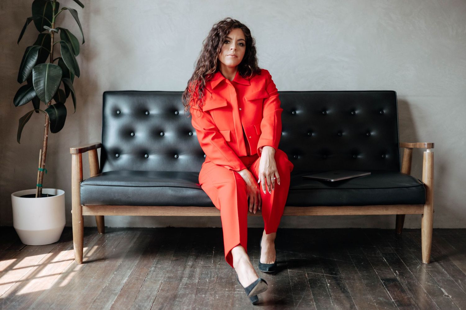 A minimalist studio session with a red outfit and black leather couch.