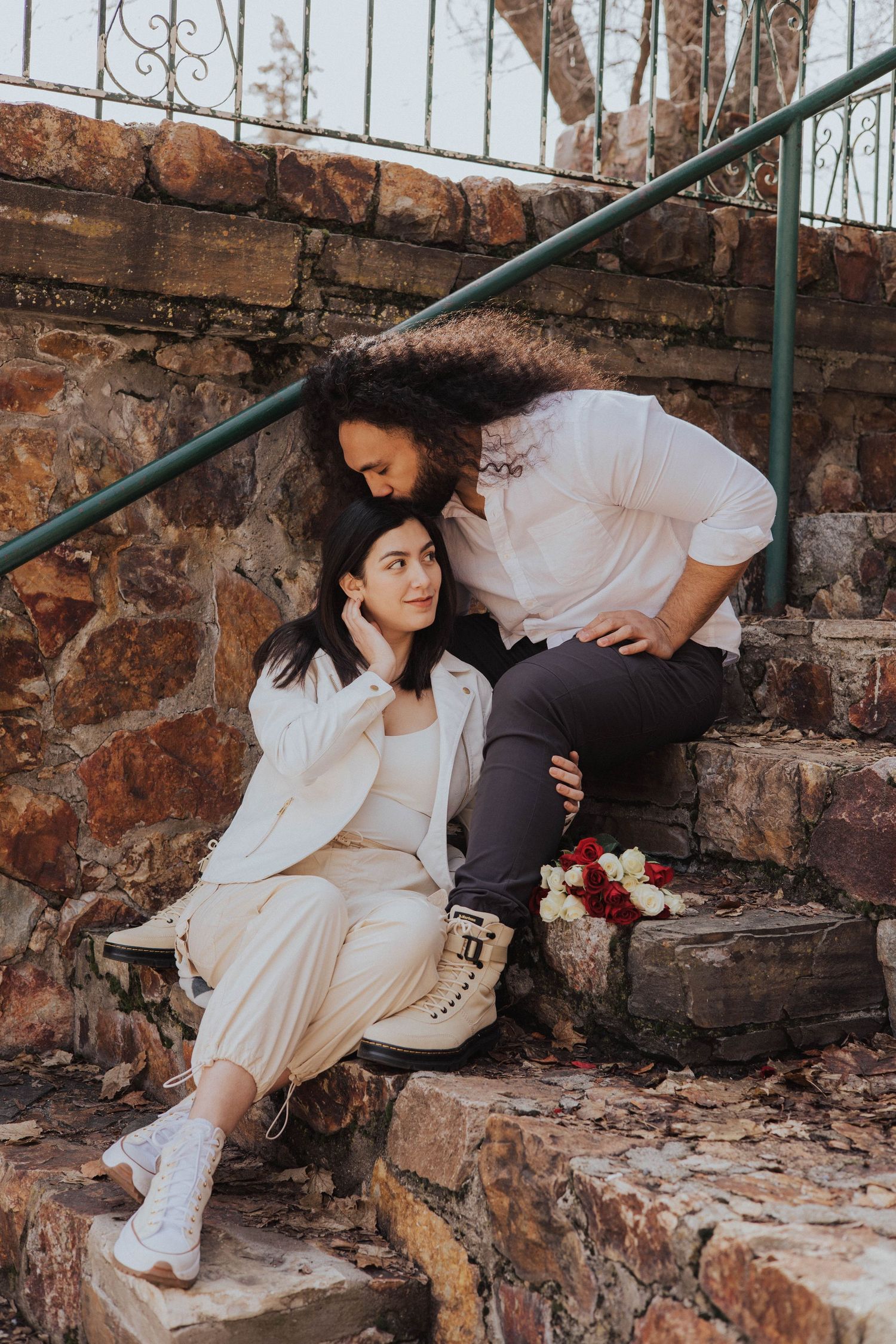 Couple posing on rustic stone steps with vintage iron railing.