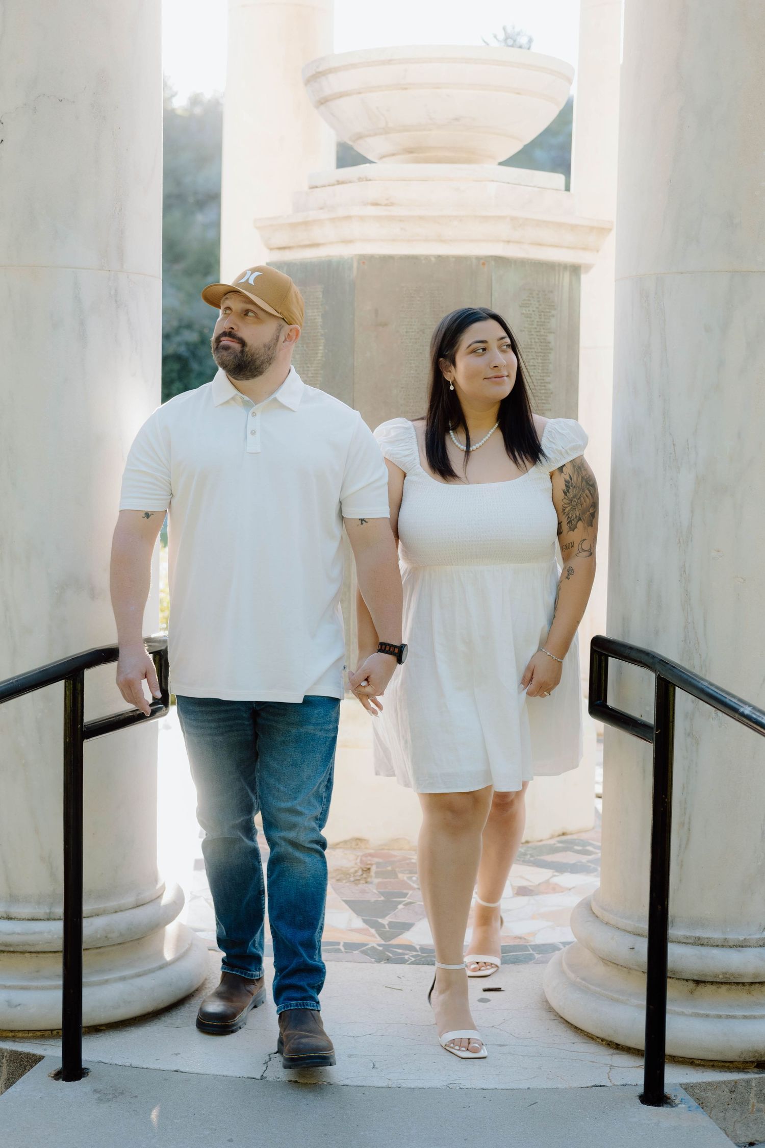 Couple standing between white classical columns in an outdoor architectural setting.