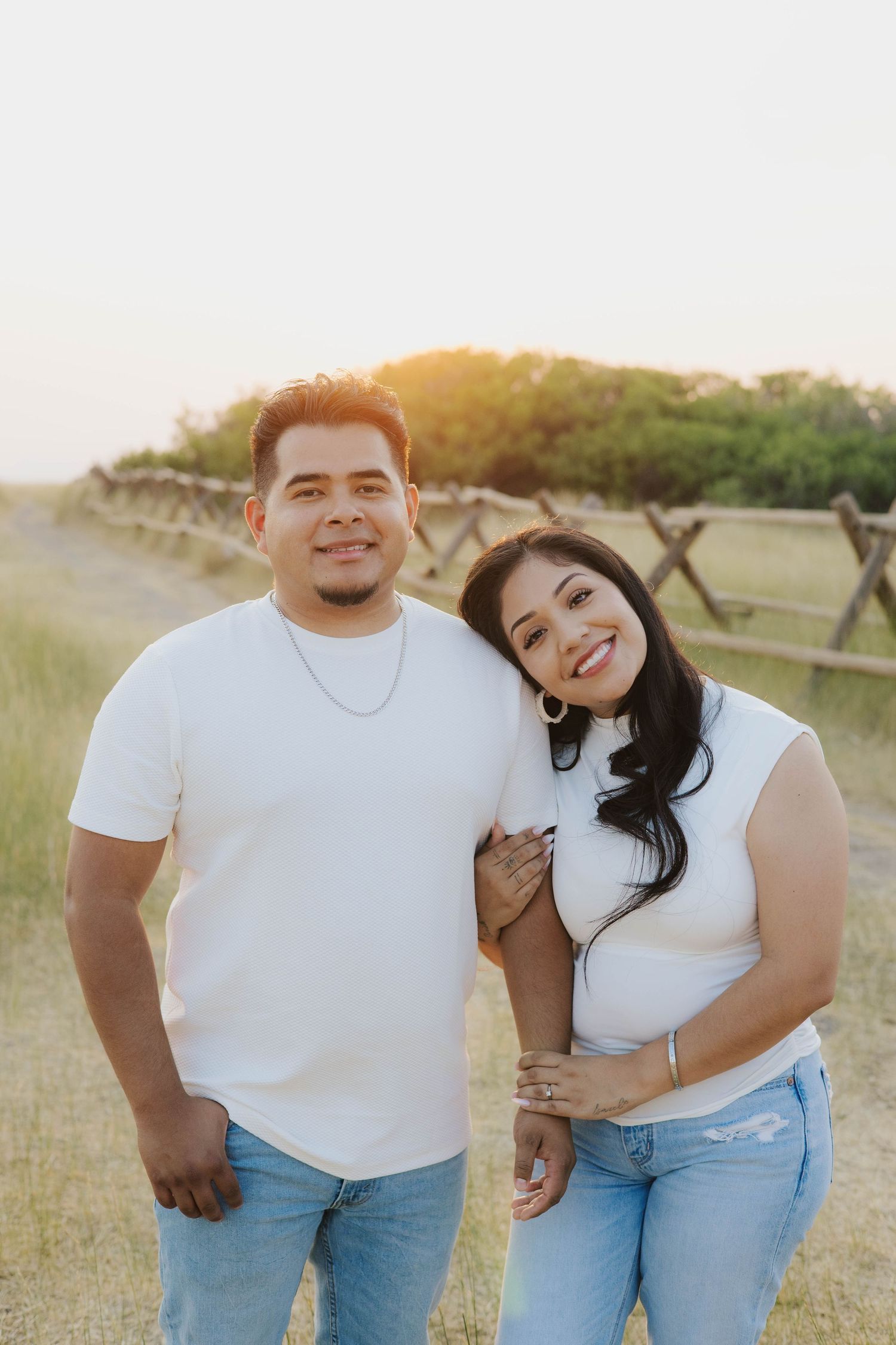 Couple in matching white tops and jeans laughing together in golden hour sunlight.