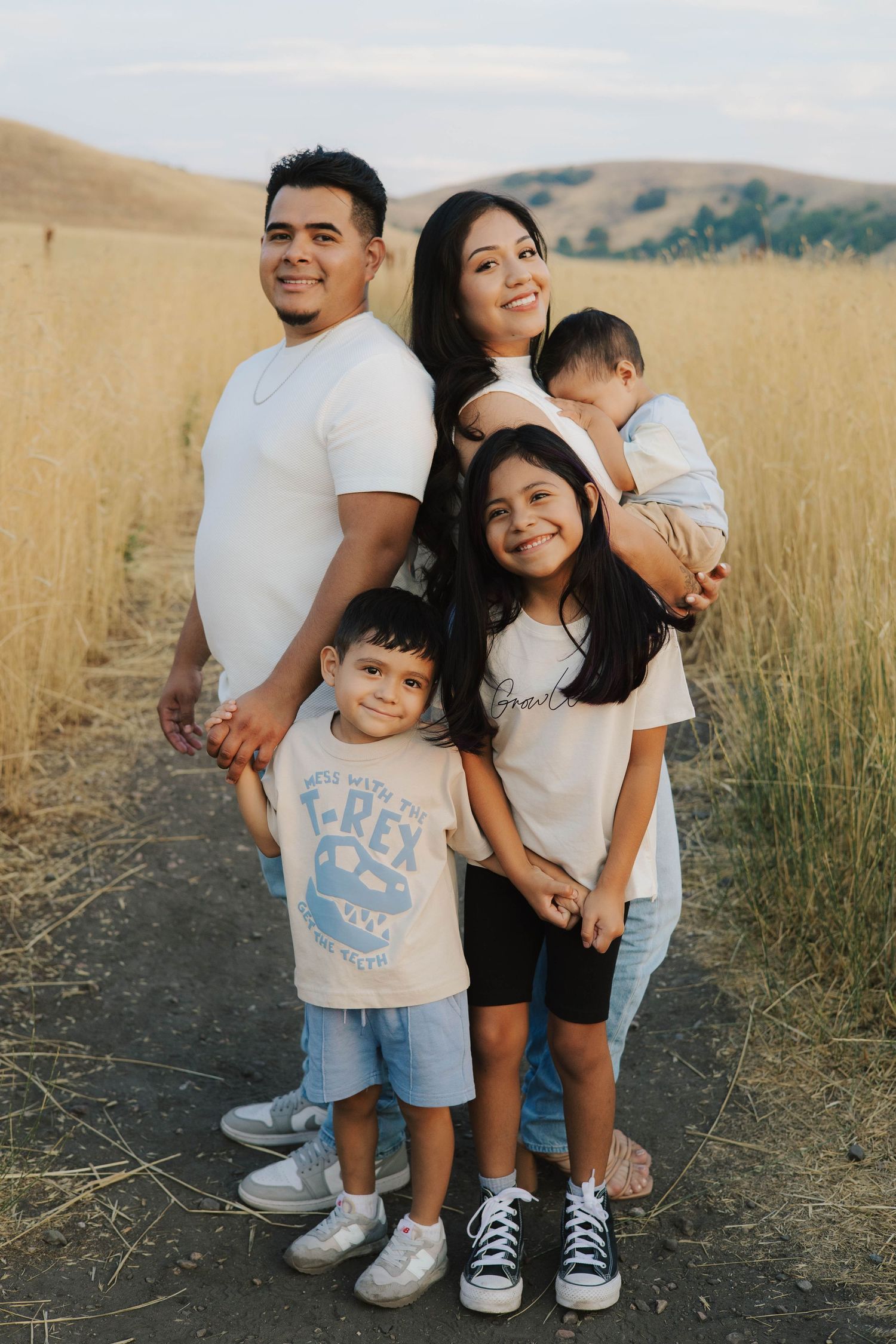 Family posing together on a trail surrounded by golden grass at sunset.