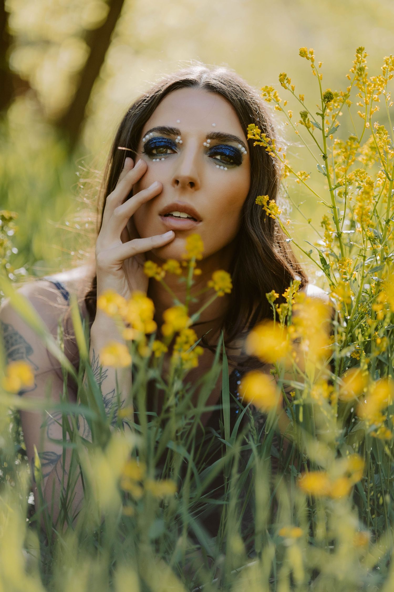 Artistic portrait among yellow wildflowers with dramatic eye makeup and natural lighting.