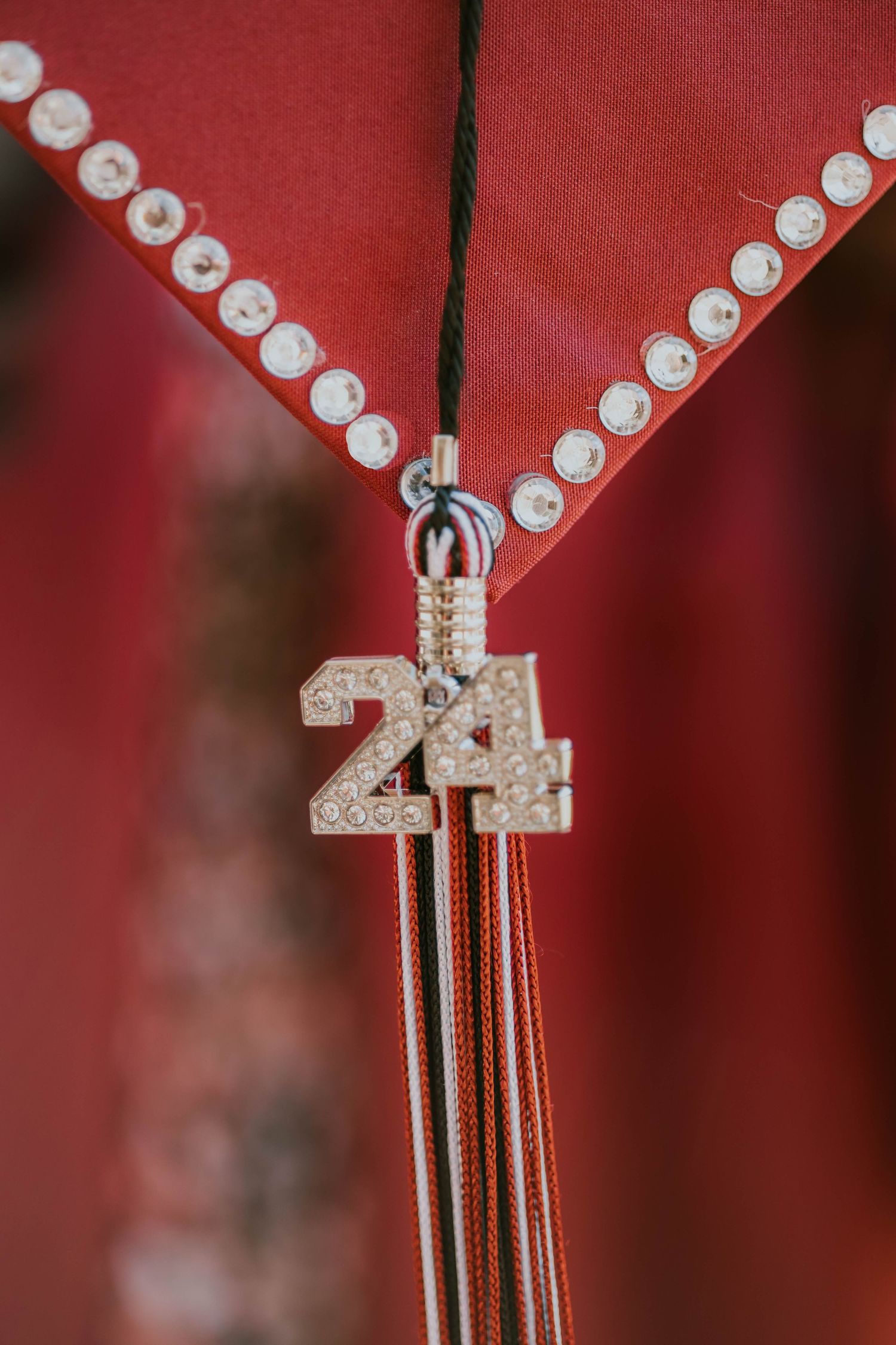 A decorative graduation cap tassel with a sparkly number 24 charm against a red background.