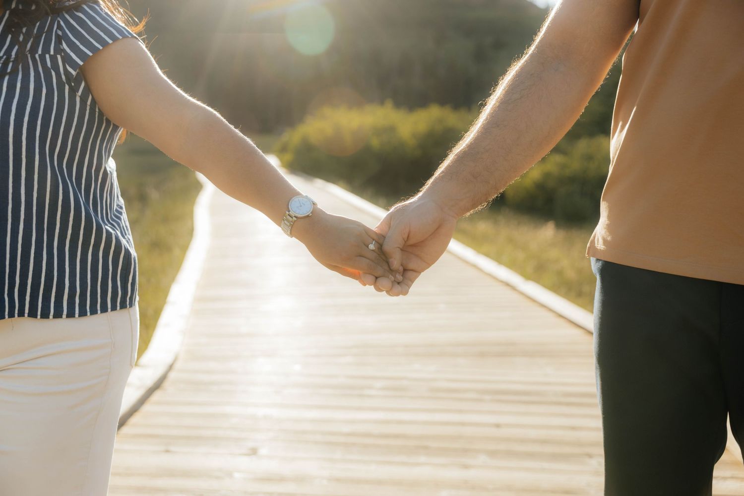 Silhouetted hands holding each other against a sunlit outdoor path.