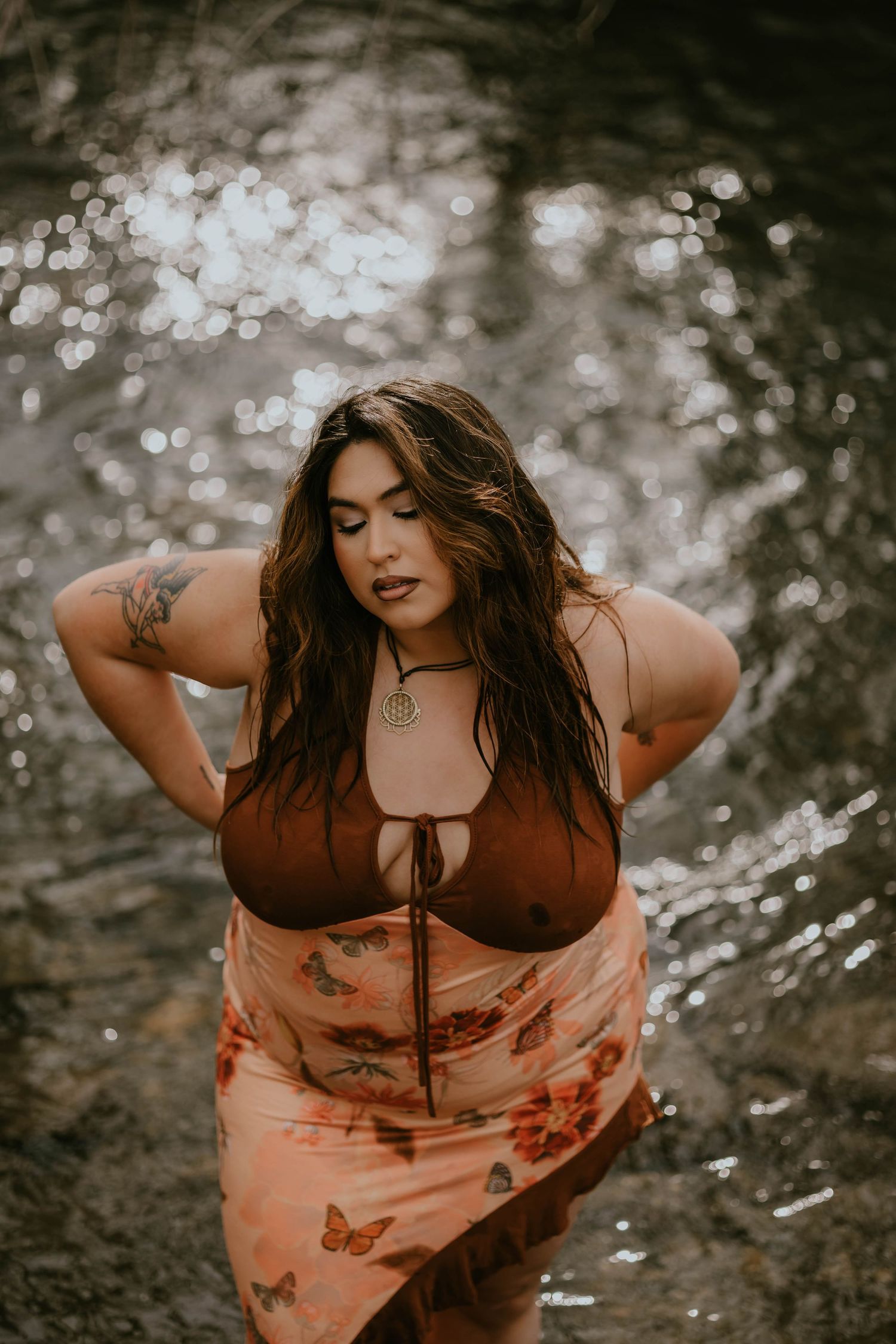 Artistic portrait by water wearing brown top and floral dress.