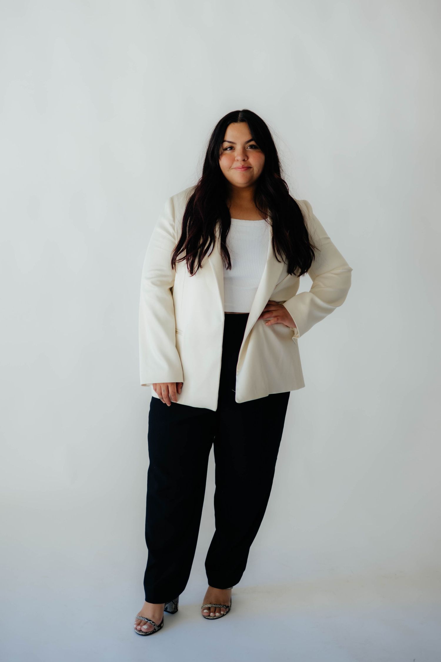 Woman in cream blazer and black pants poses confidently against white background.