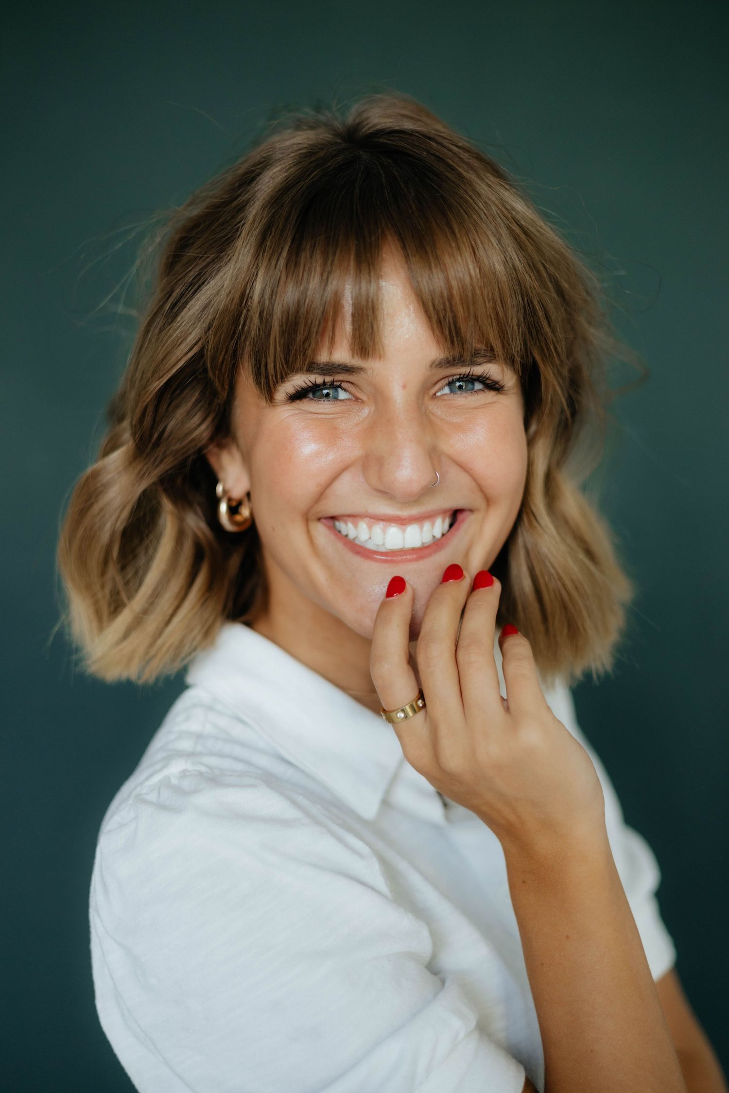 Portrait of woman in white shirt with blonde wavy bob hairstyle against green background.