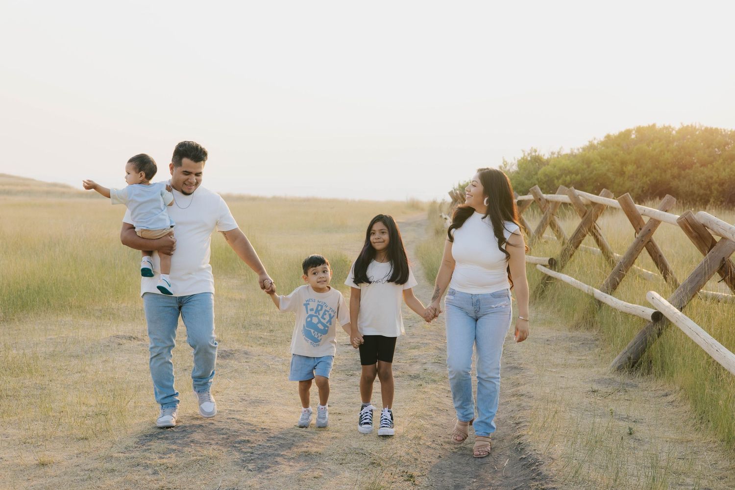 Family walking together holding hands along a rustic fence at sunset.