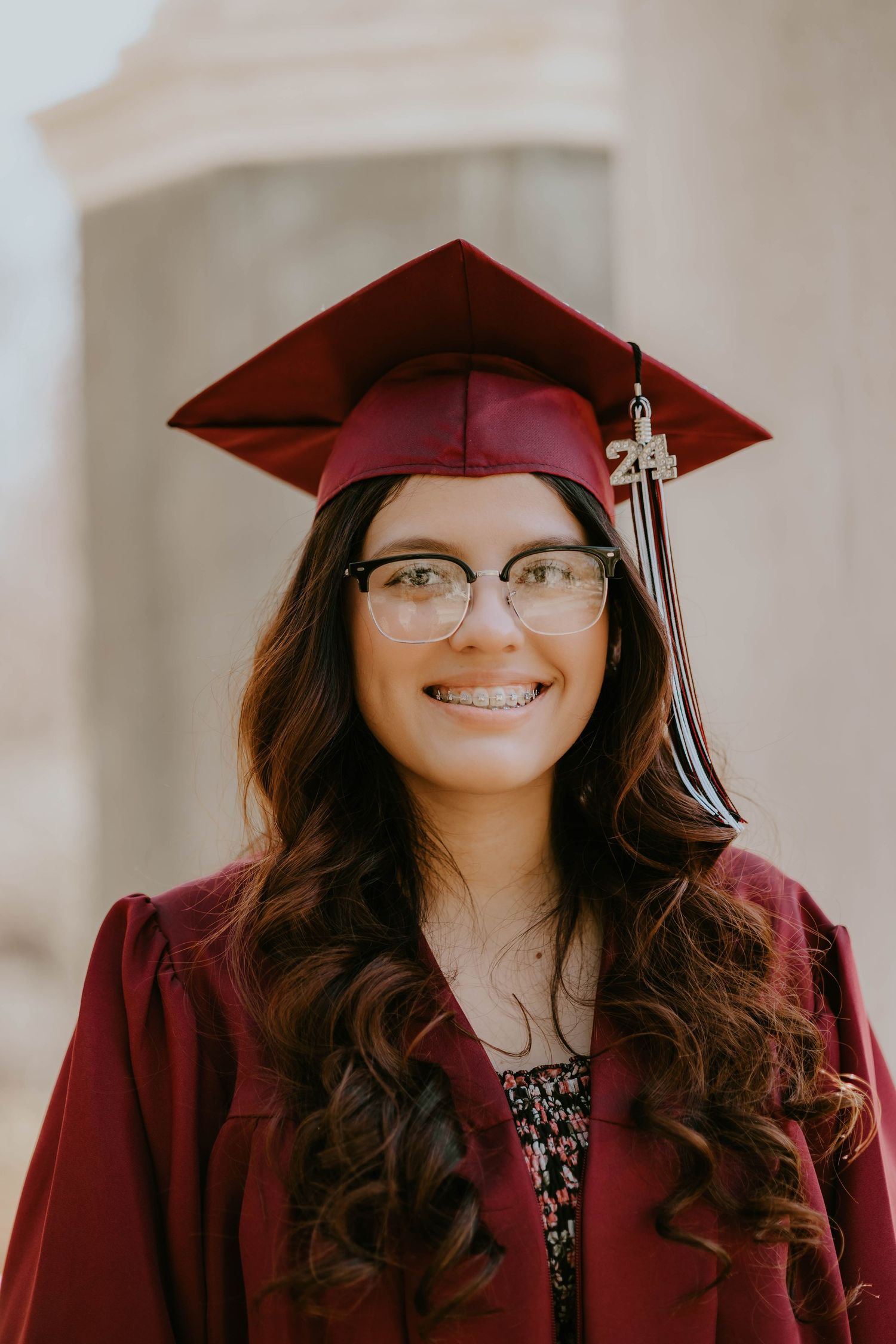 Graduate in red cap and gown smiling against light background.