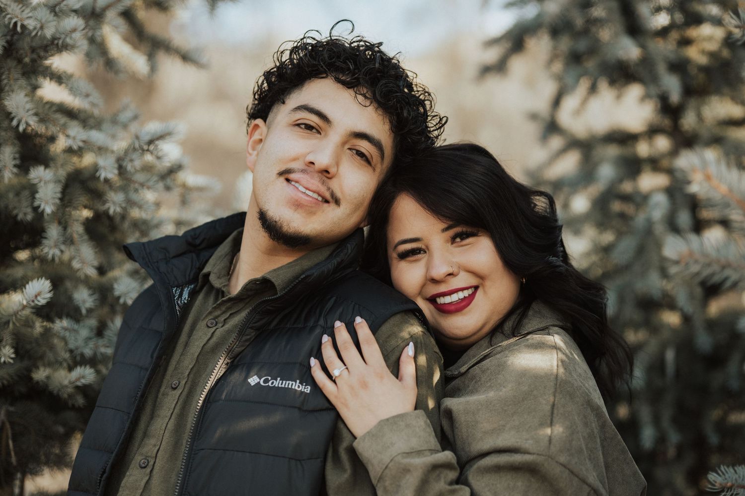 Happy couple posing together outdoors with evergreen trees in background during winter season.