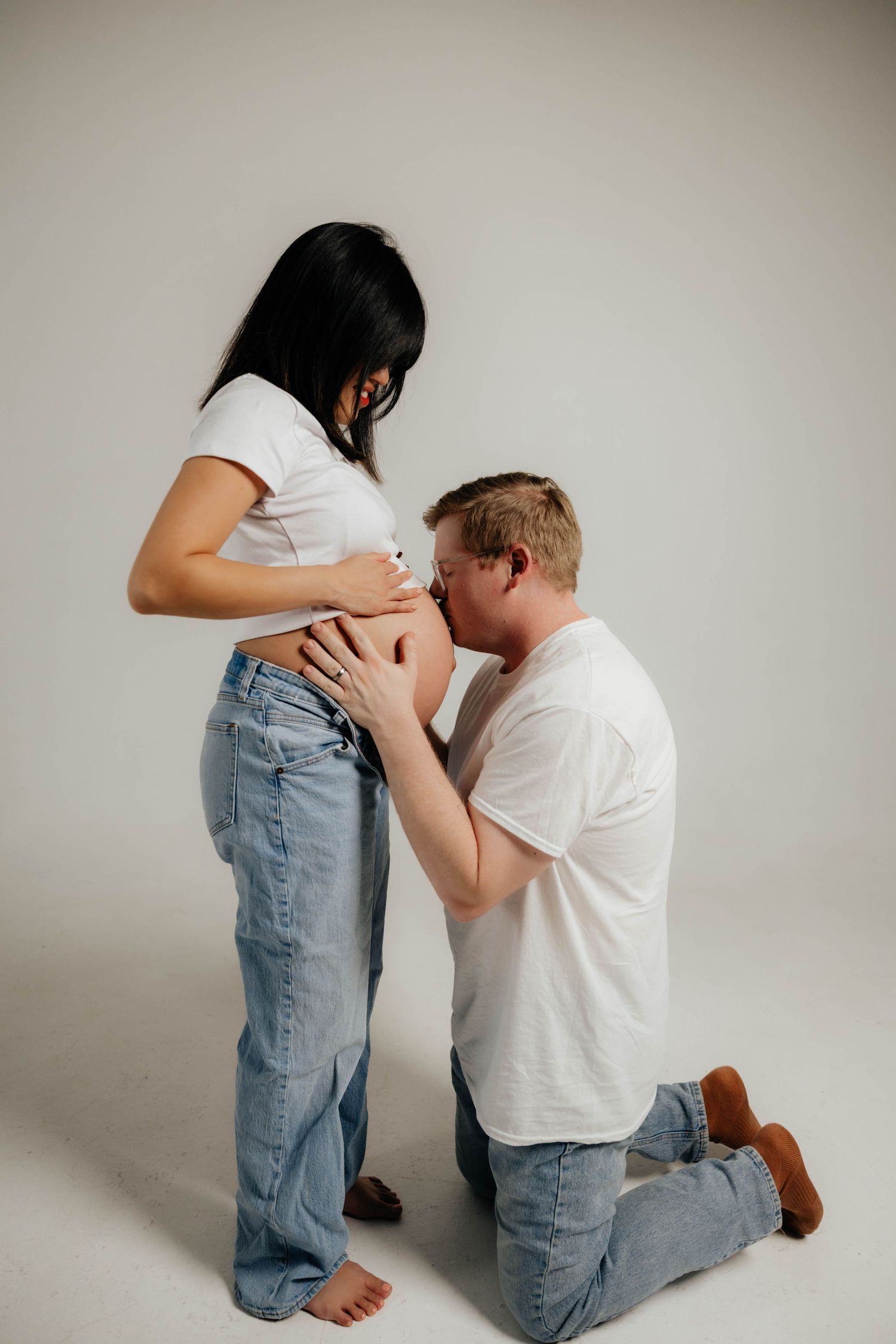Intimate maternity studio photos with emotional moments captured against white backdrop.