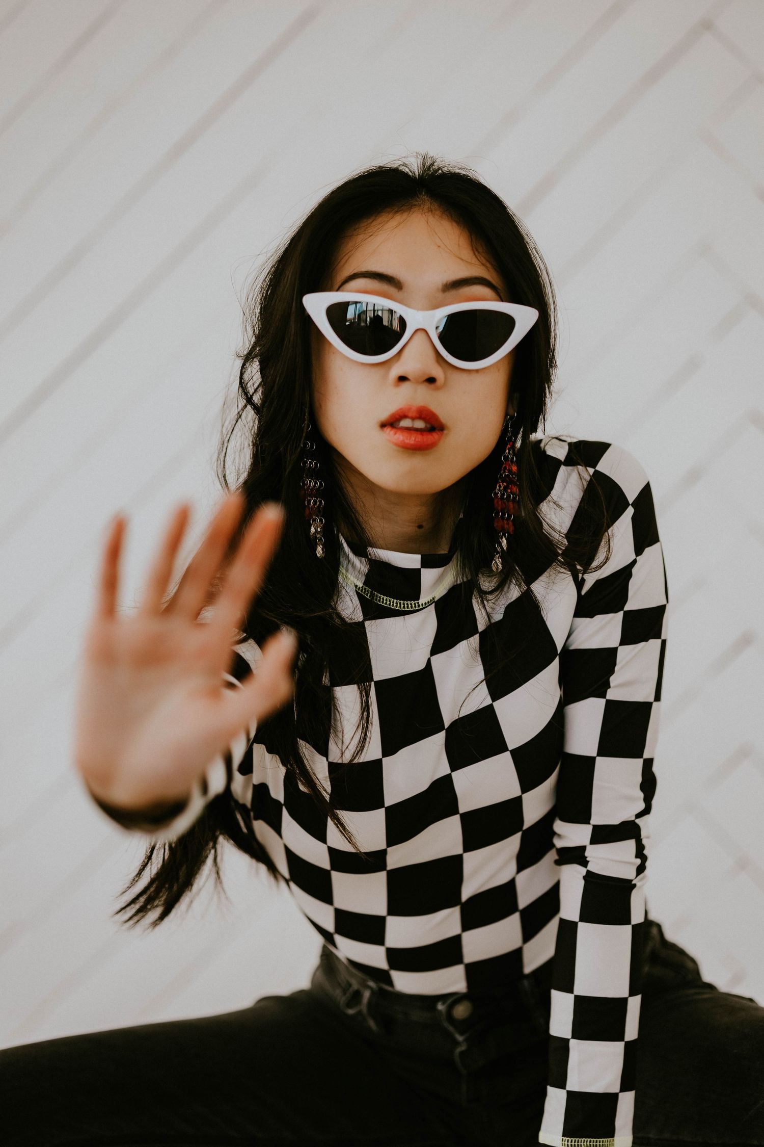 Stylish fashion photoshoot featuring checkered jacket and white cat-eye sunglasses against light background.