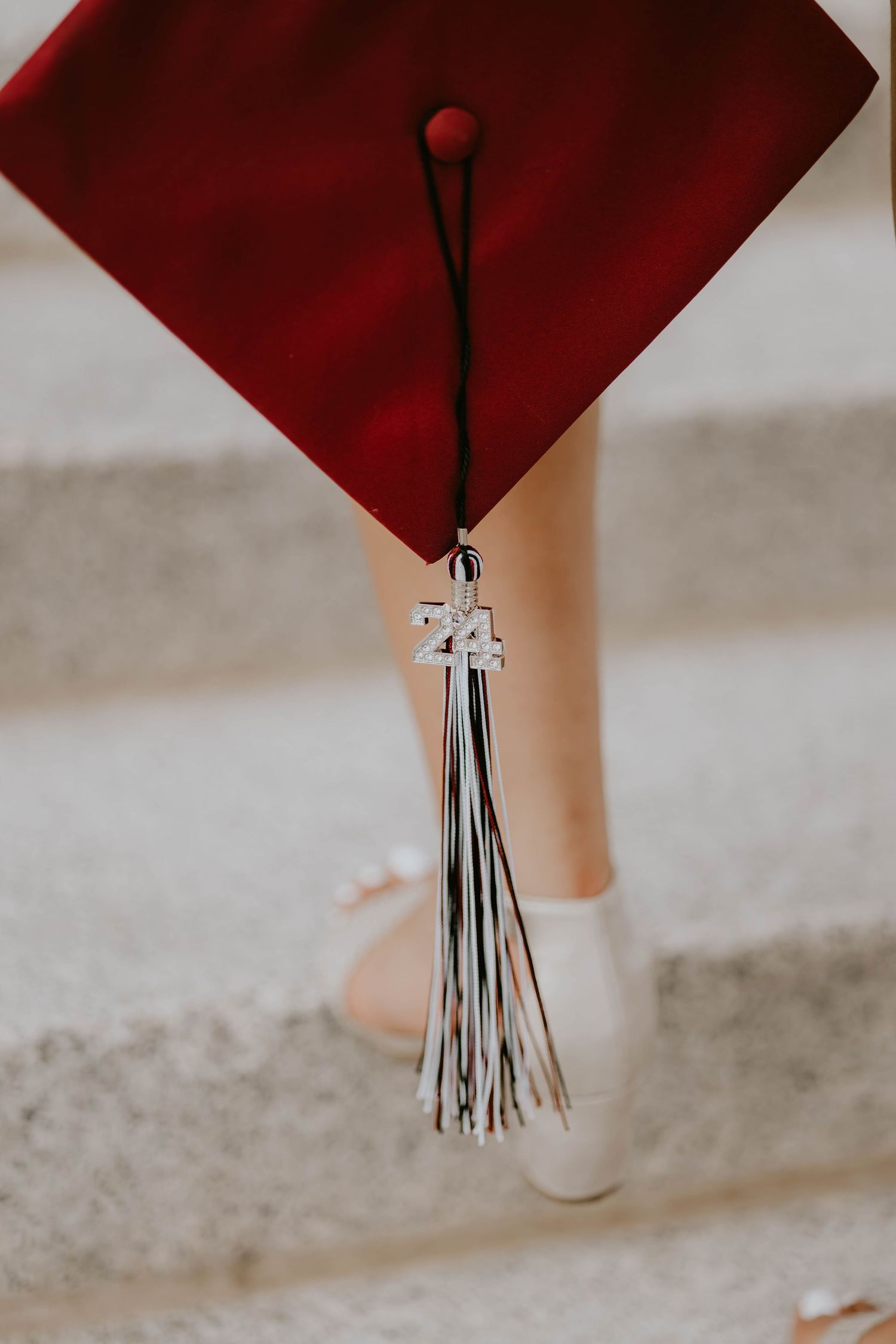 A red graduation cap with silver tassel and class of 24 charm shown in detail.