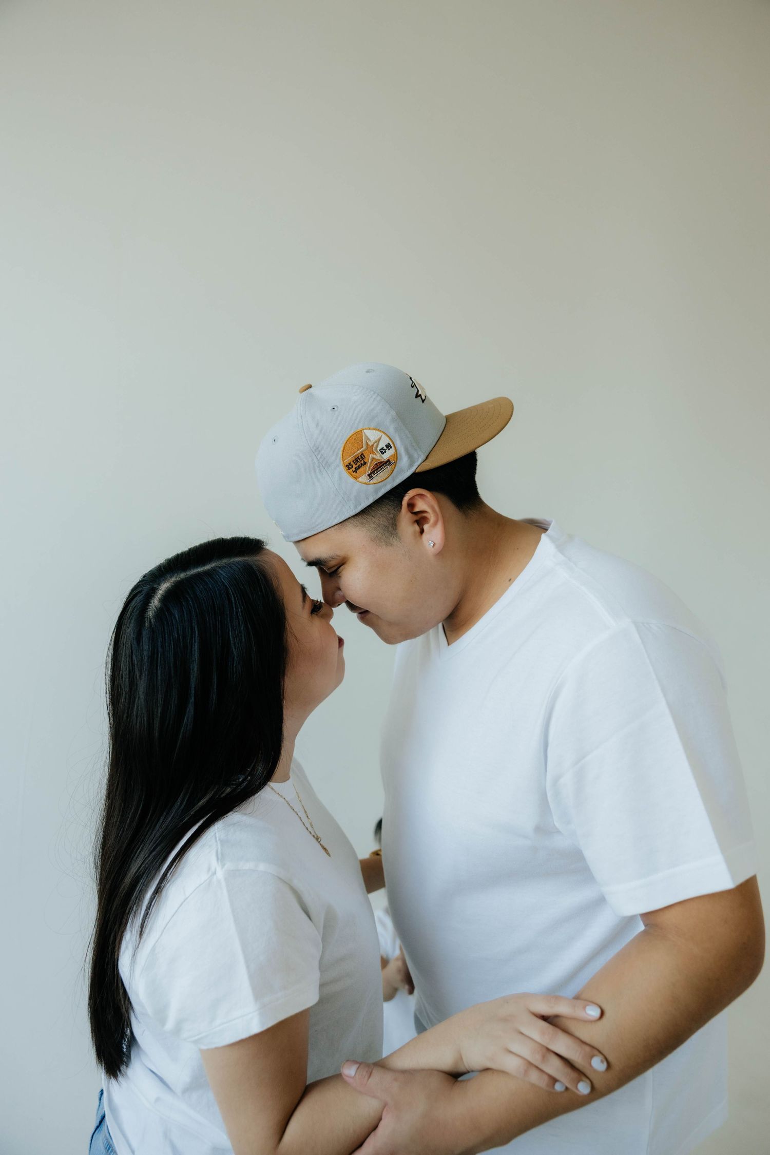 Couple in matching white outfits sharing an intimate moment against a plain wall.