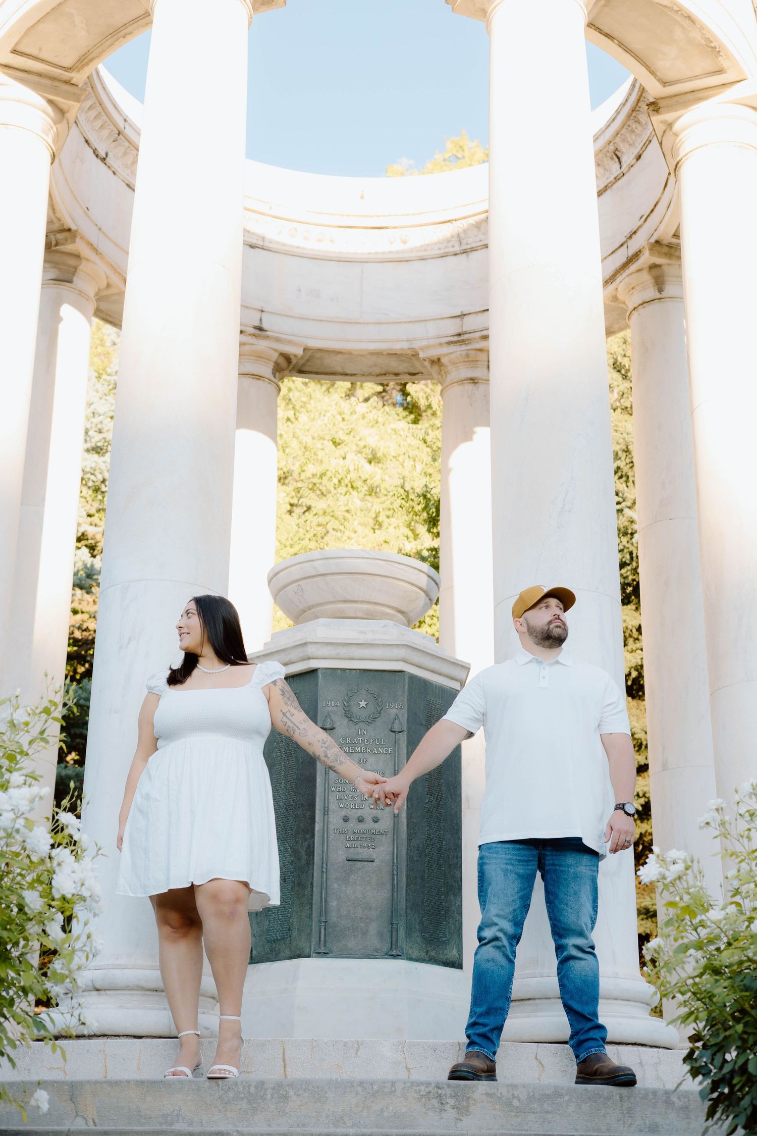 Couple posing between white pillars in a garden gazebo setting.