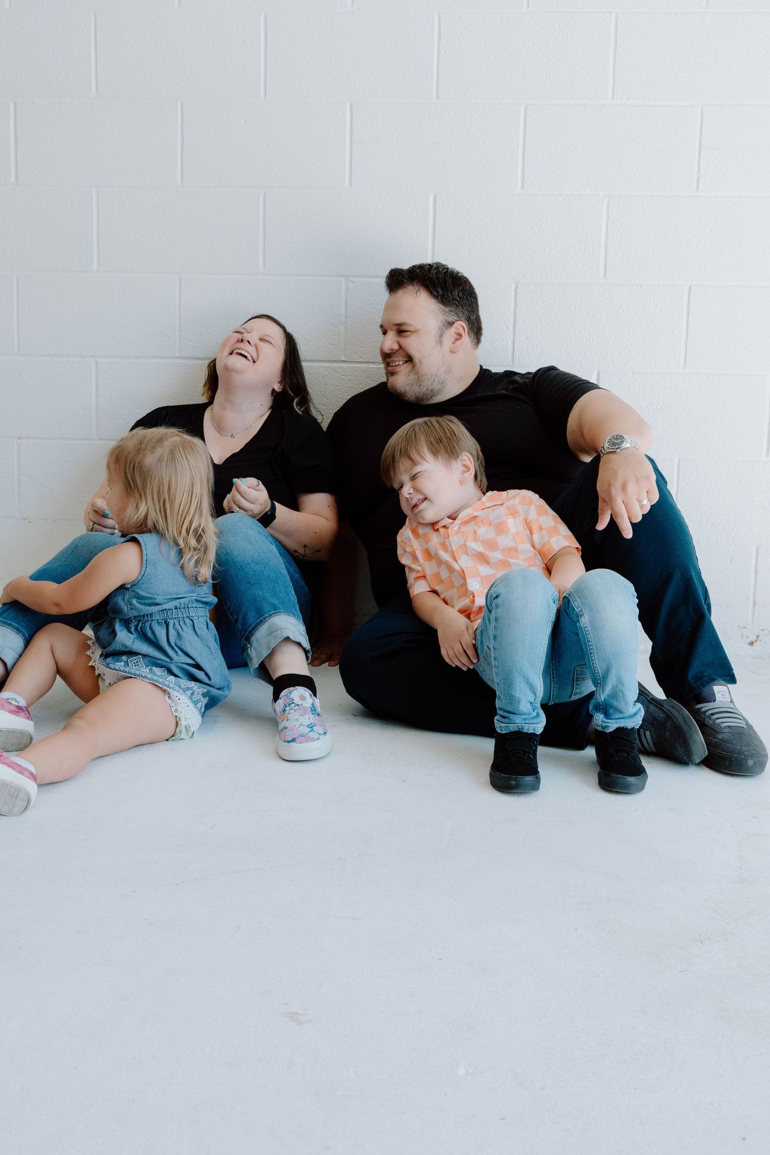 Family lying together on white floor in casual studio photoshoot.