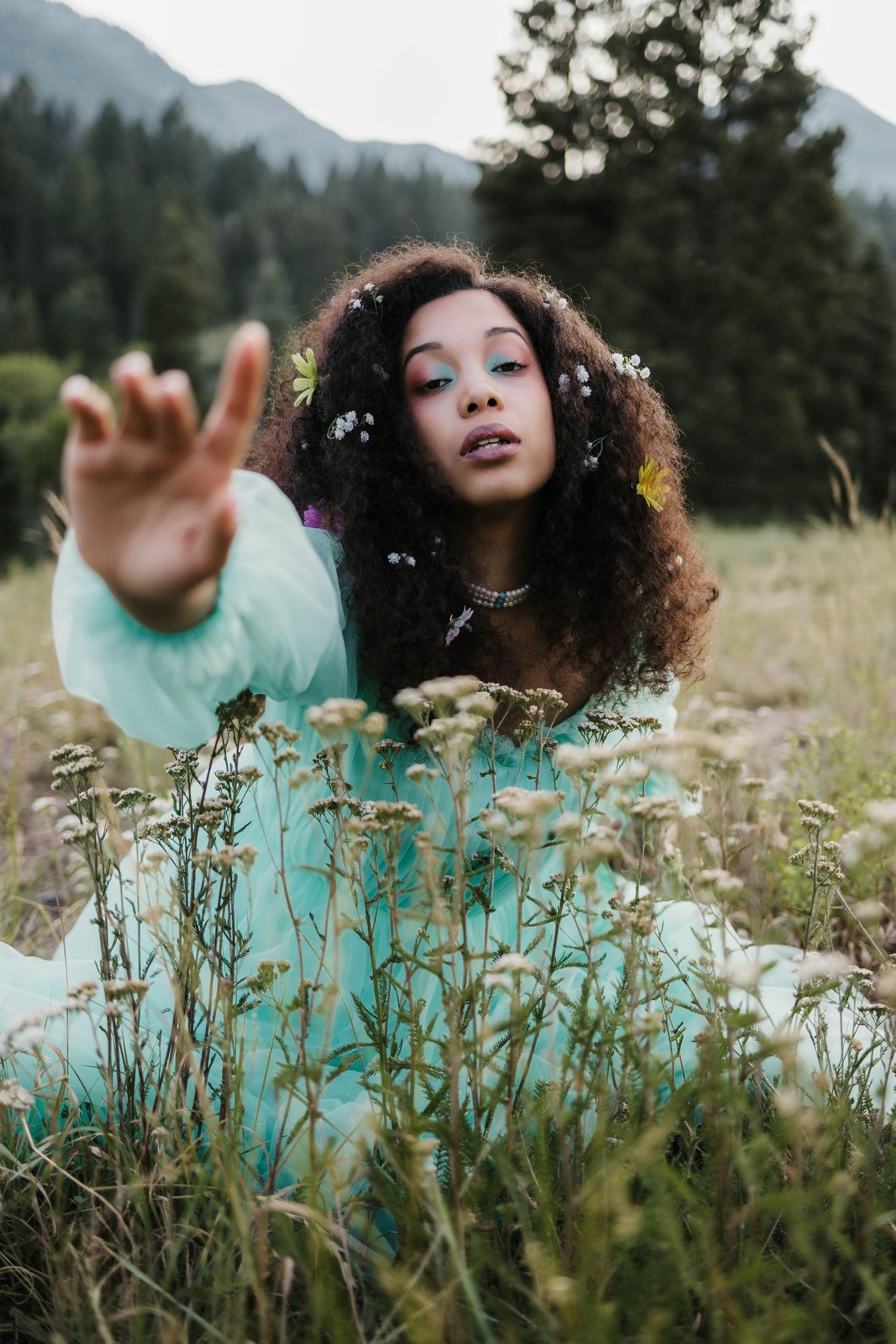 Ethereal portrait in a mint dress lying in a mountain meadow with wildflowers.