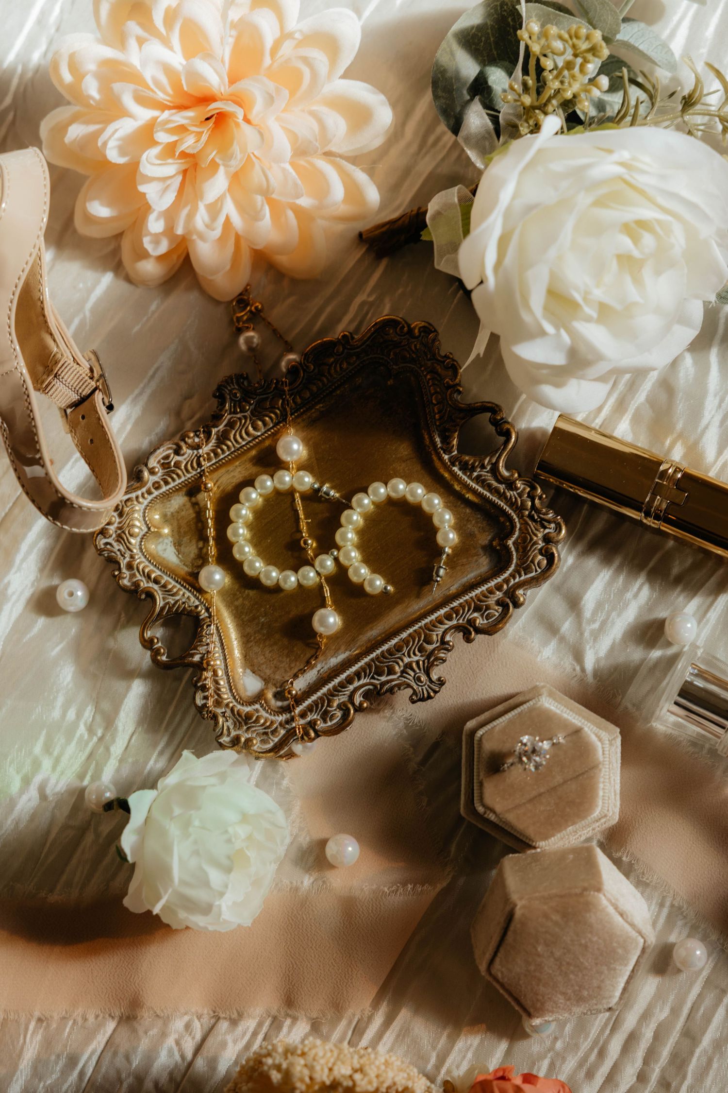 Elegant wedding details with pearls, flowers and vintage accessories on wooden surface.