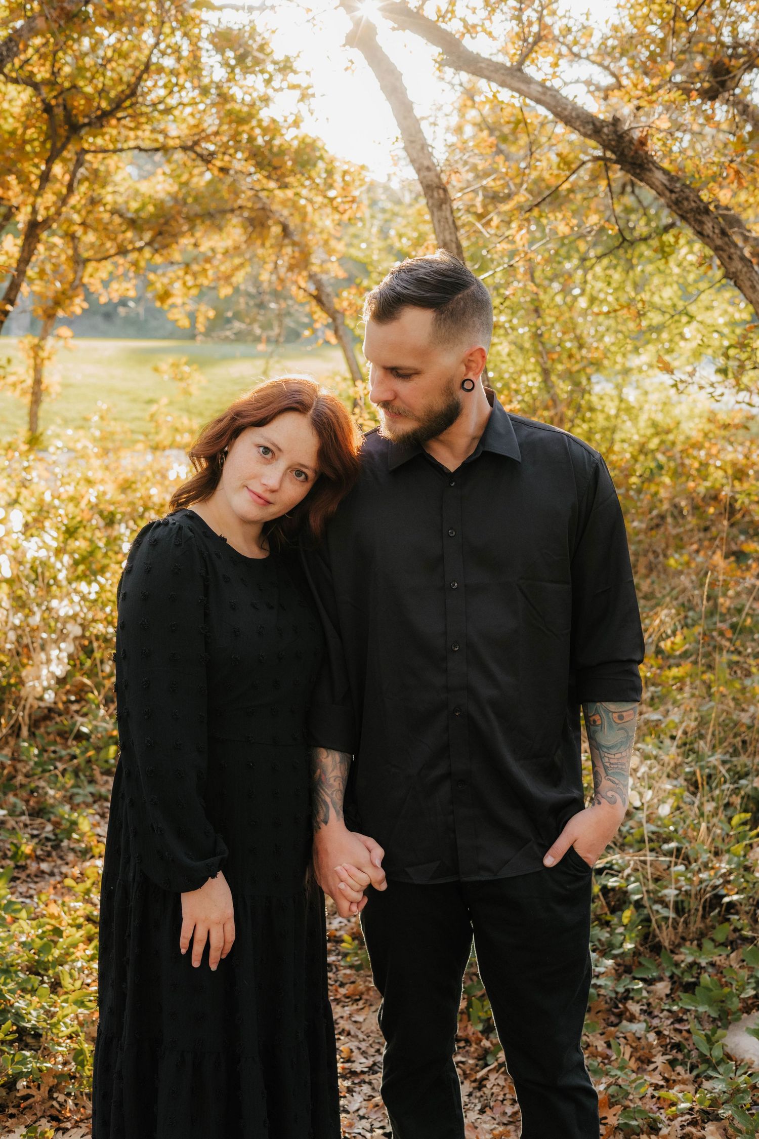 Couple in black attire holding hands during golden hour in autumn forest setting.