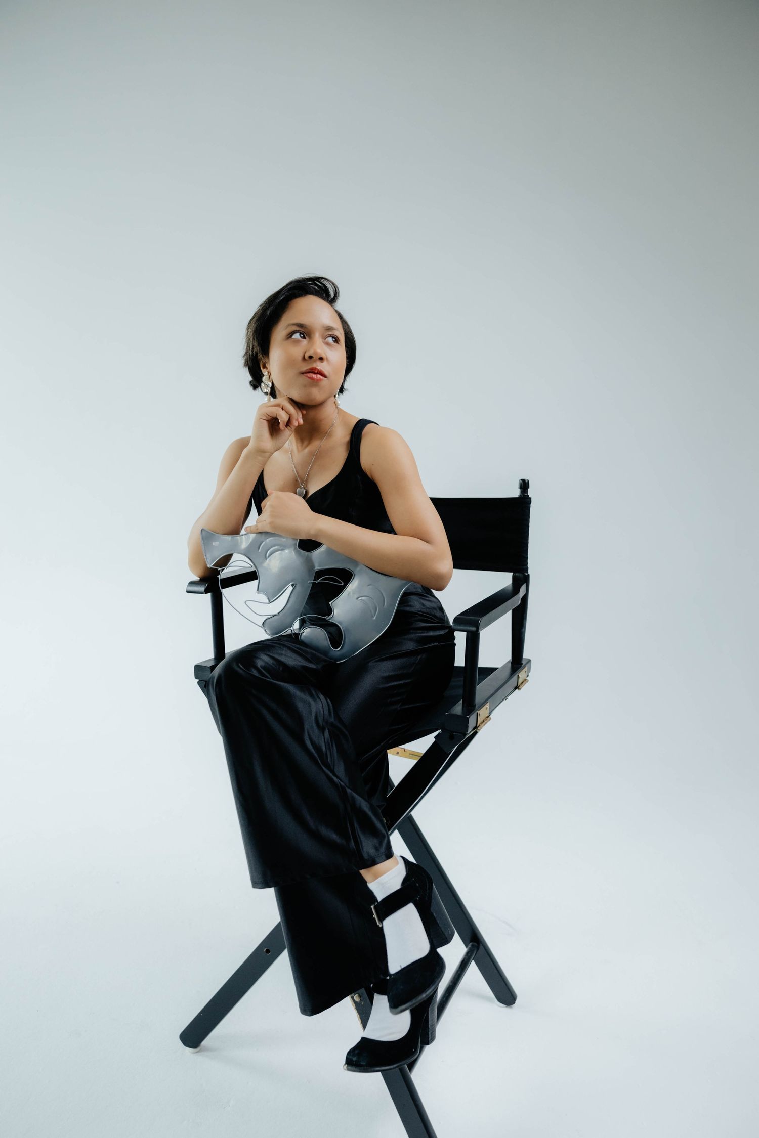 Modern portrait series showing someone posed thoughtfully in a director's chair against white backdrop.