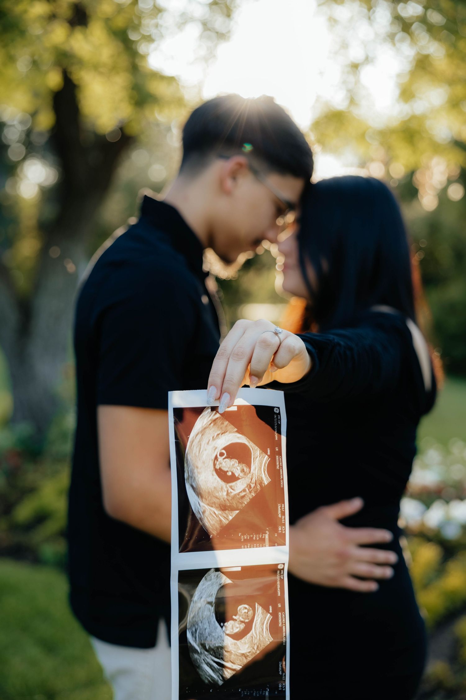 Couple holding ultrasound photos during sunset pregnancy announcement photoshoot.