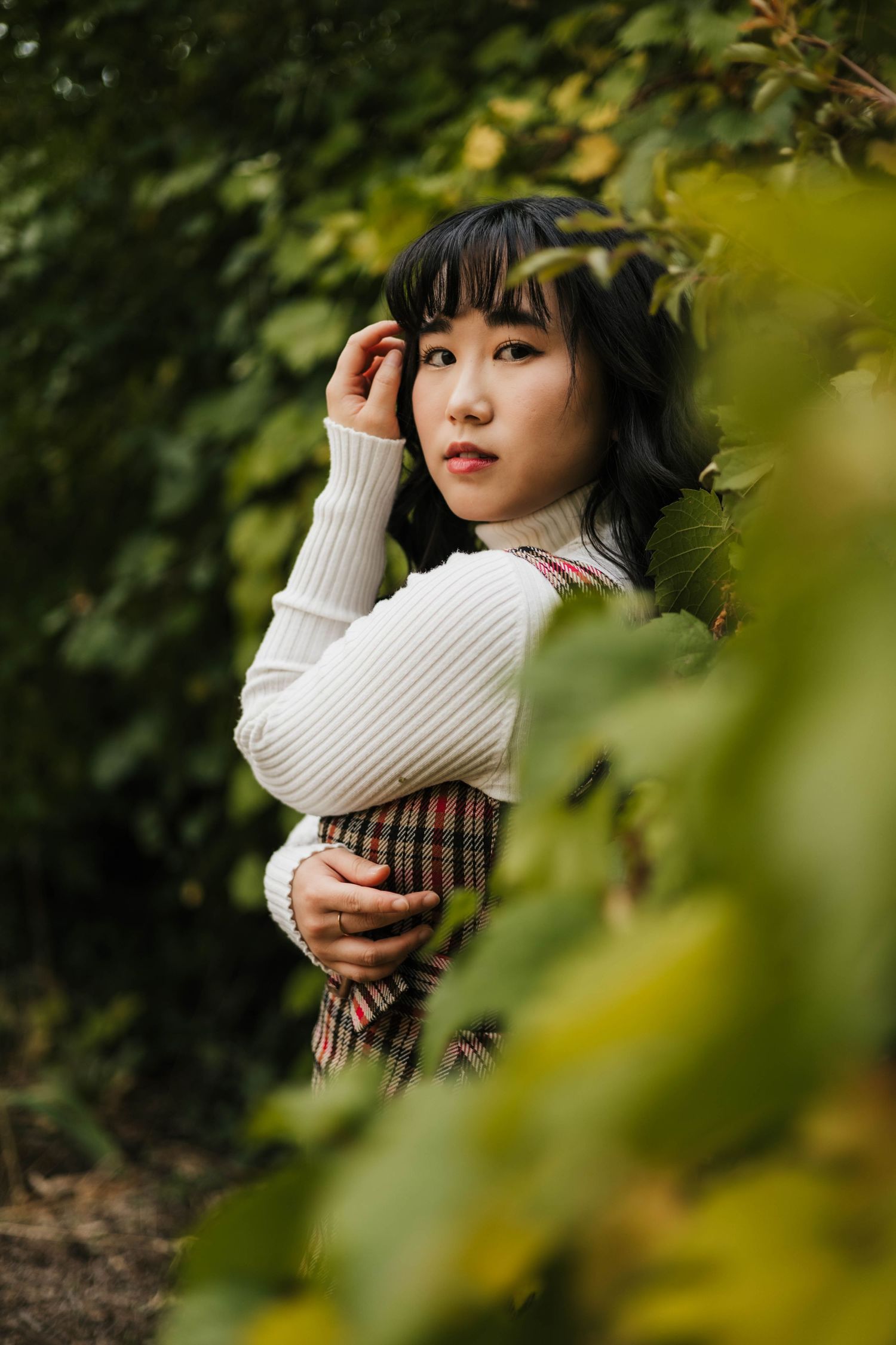 Portrait series through foliage featuring cream sweater and natural lighting.